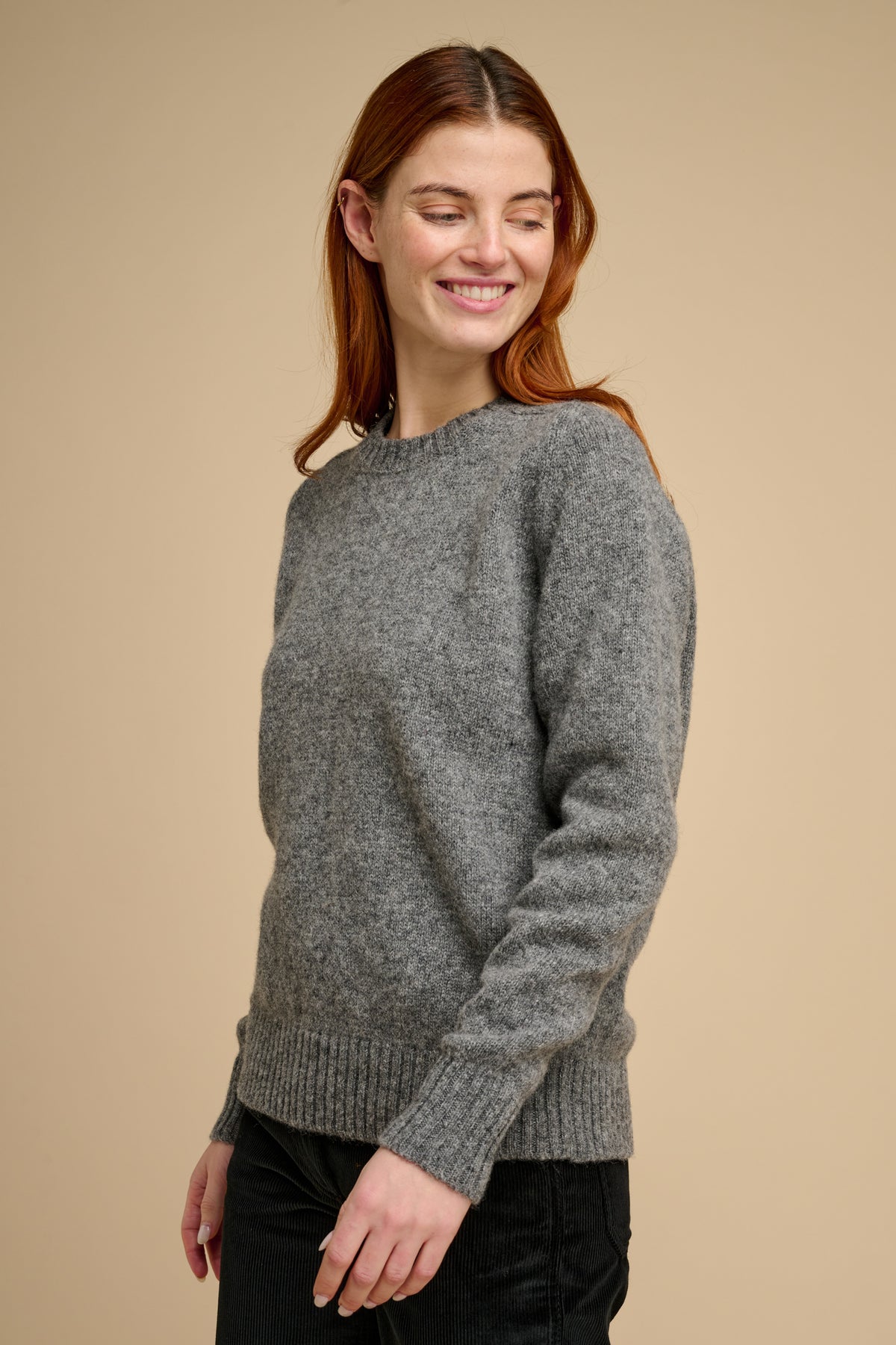 Woman wearing knit jumper in grey against a beige background.