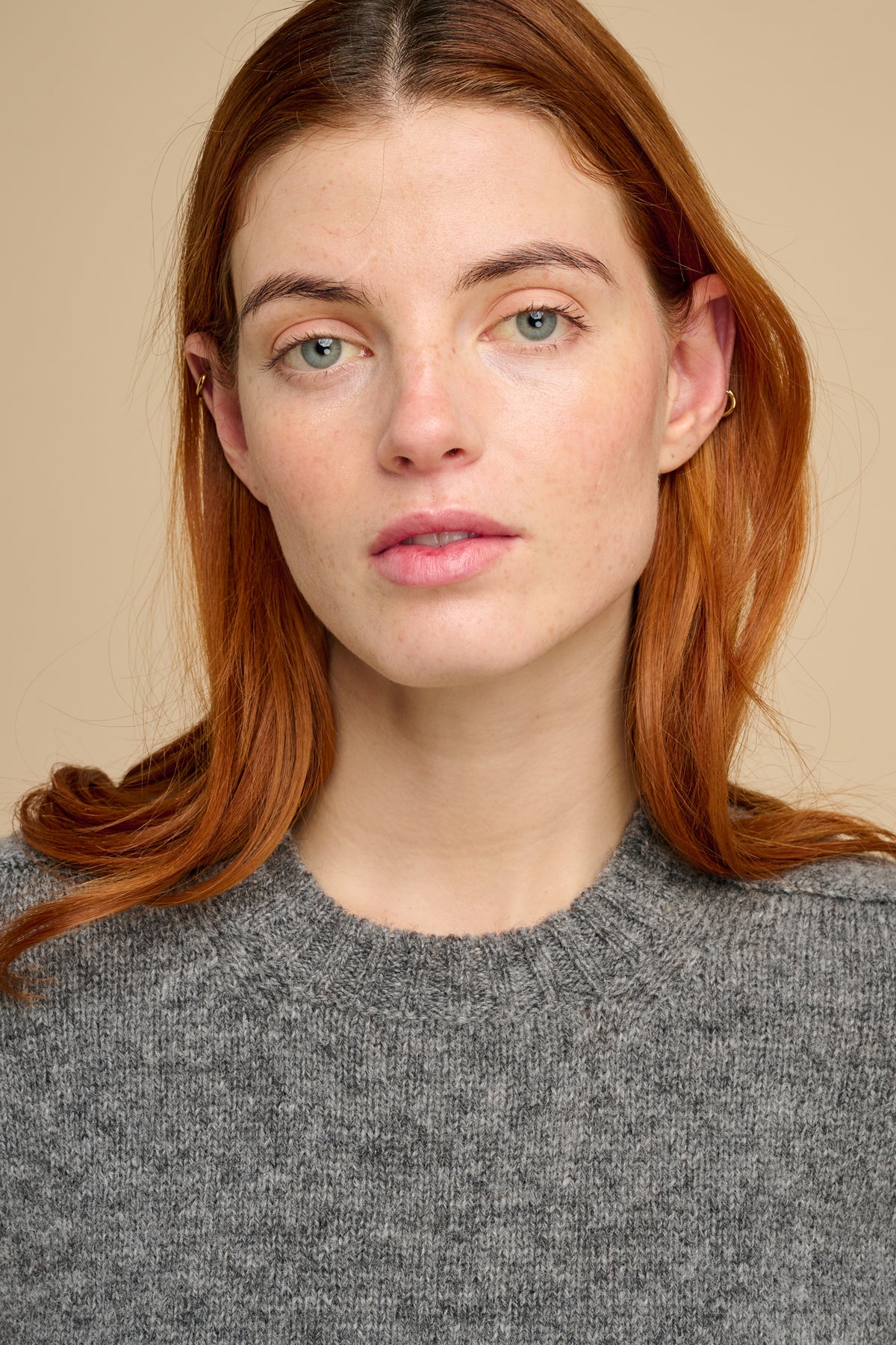 Woman with red hair wearing a gray sweater against a beige background