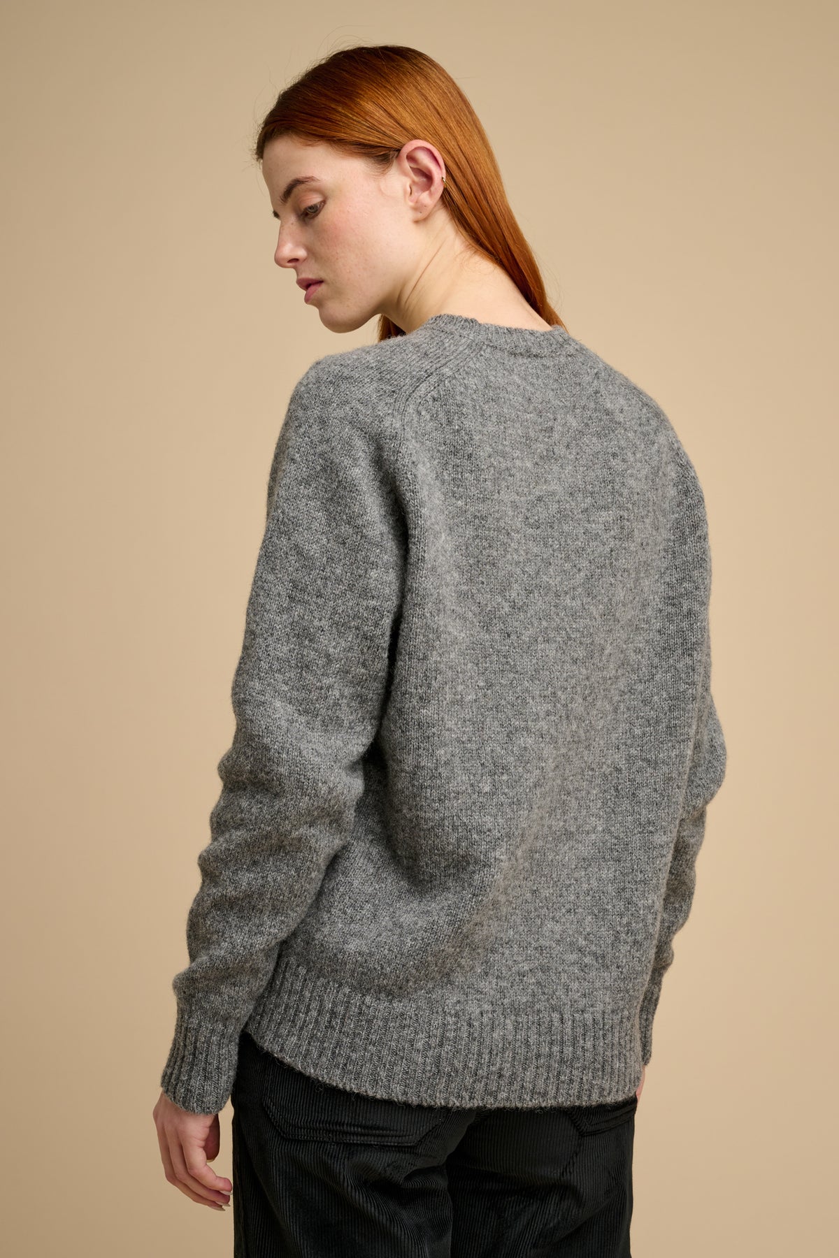 The back of woman wearing knit jumper in grey against a beige background.