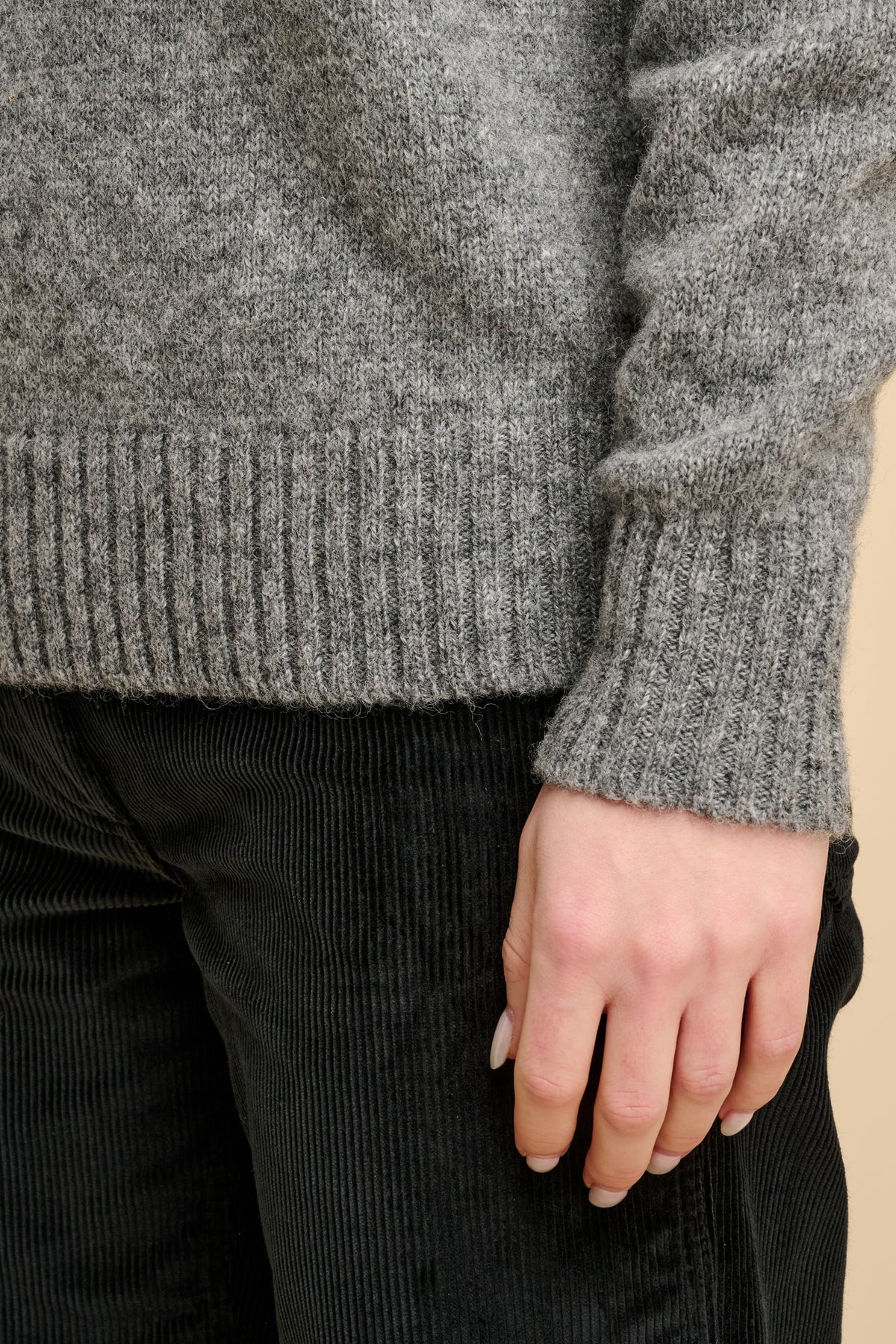Close up of the ribbed cuff and hem of grey knit jumper and black corduroy trousers.
