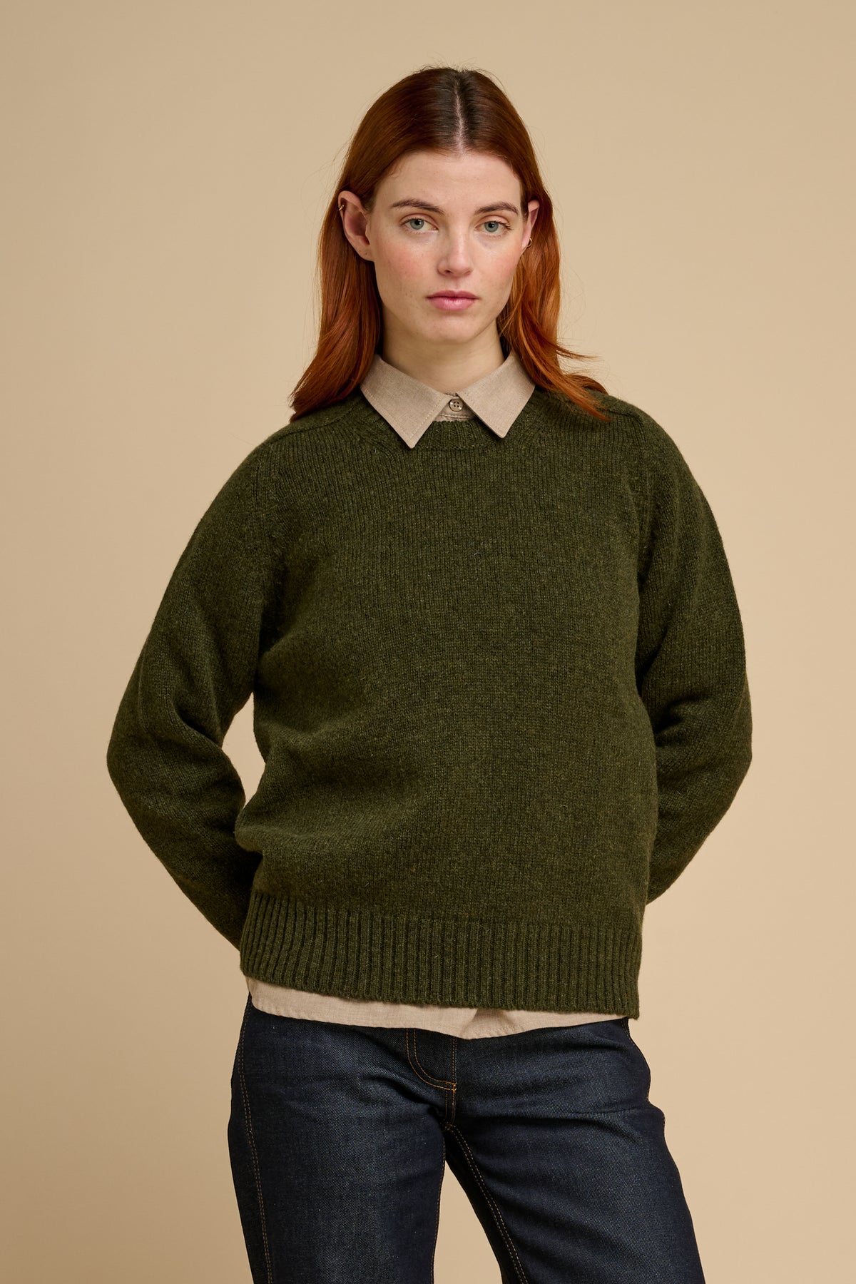 Woman wearing a green sweater over a collared shirt with a beige background