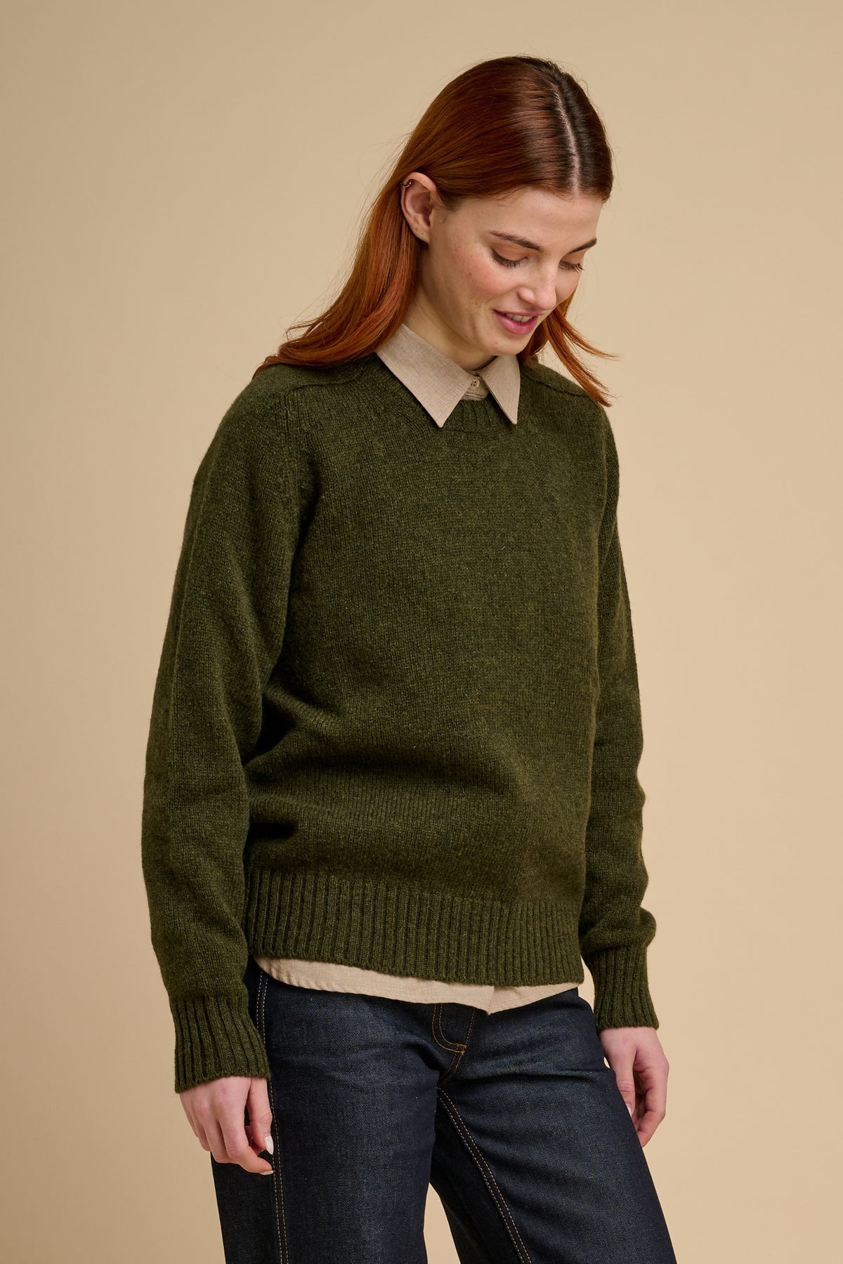 Woman wearing a green sweater over a collared shirt with a beige background