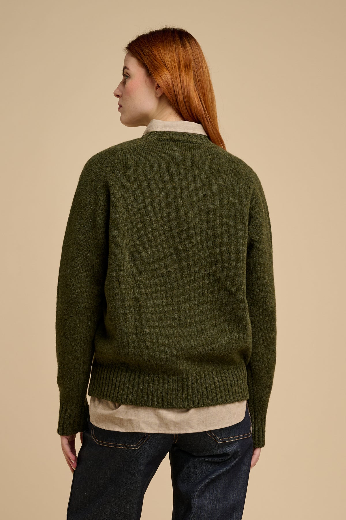 Woman wearing a green sweater over a collared shirt with a beige background