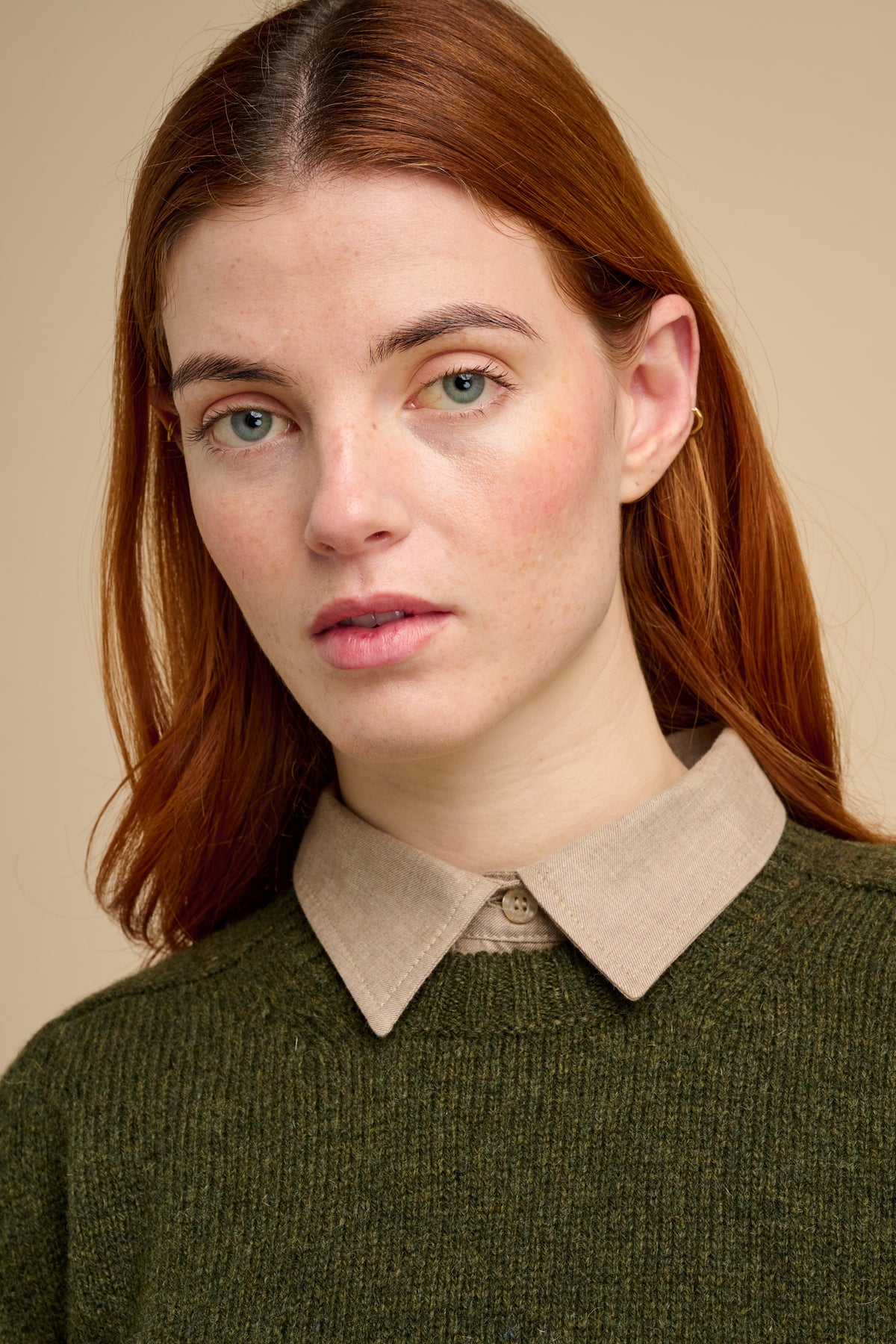 Woman wearing a green sweater with a beige shirt collar against a beige background.