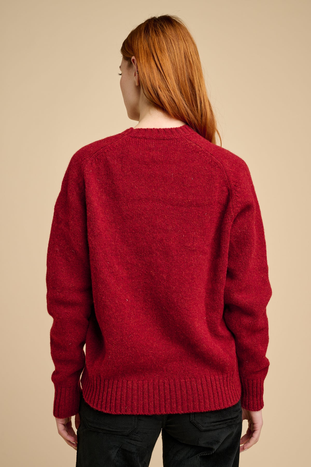 The back of a woman wearing a red sweater on a beige background