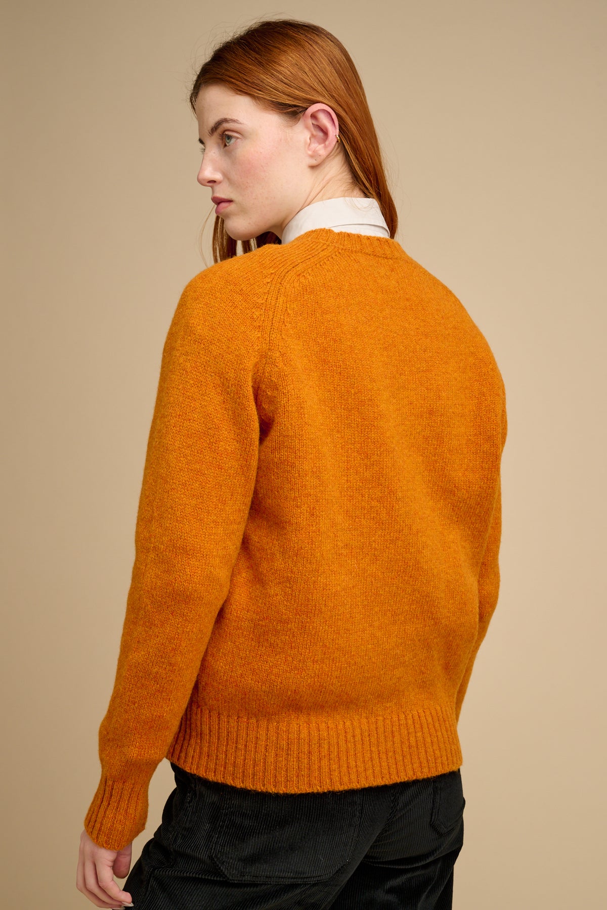 Person wearing an orange sweater against a beige background