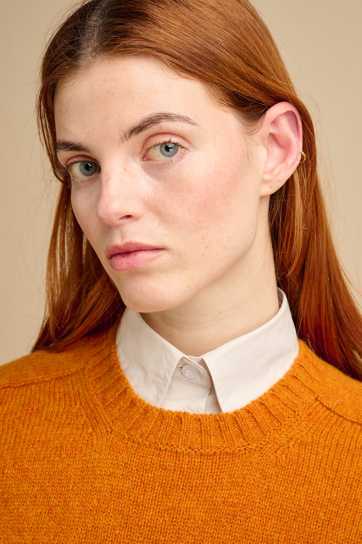 Person wearing an orange sweater over a white shirt against a beige background
