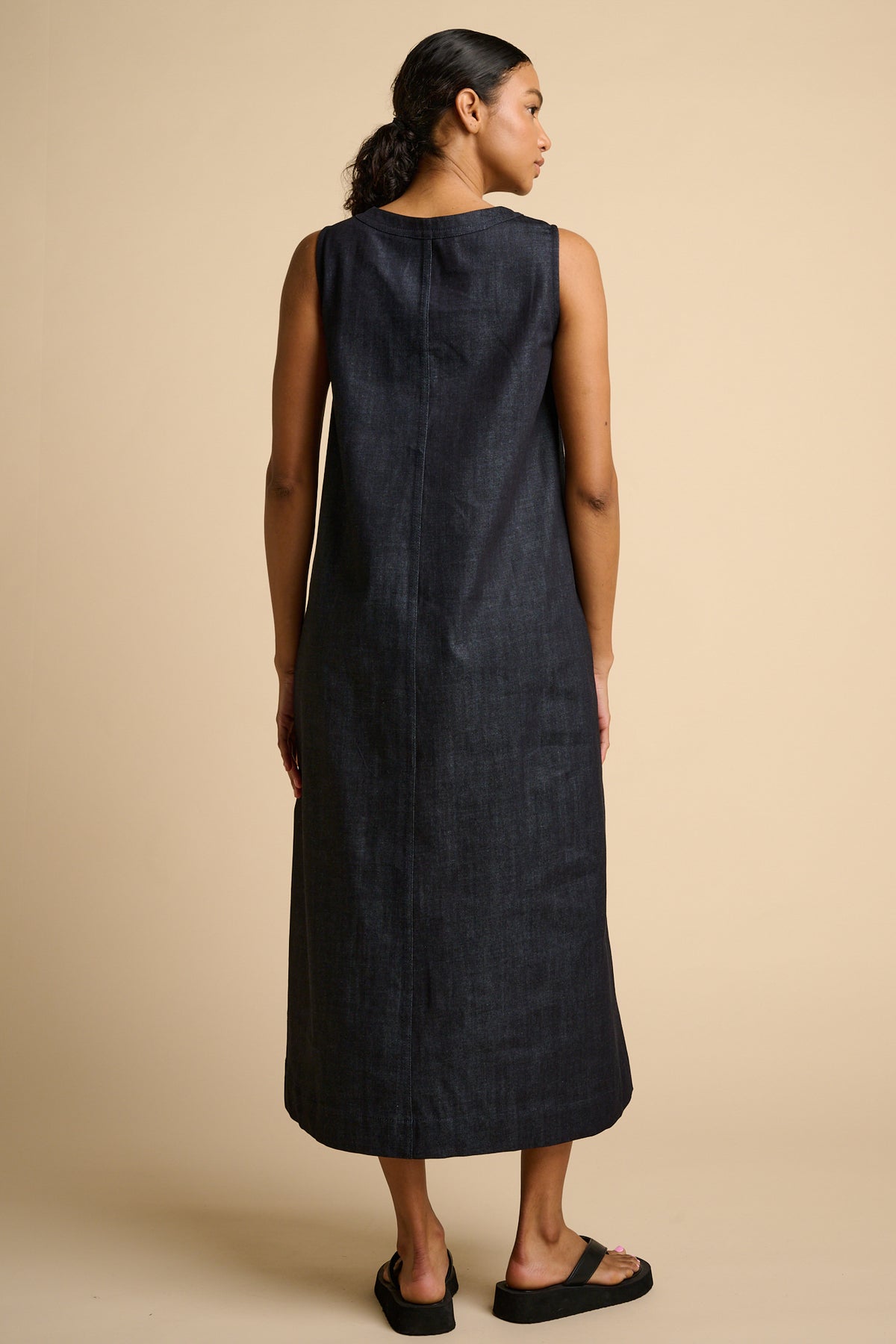 Woman wearing indigo sleeveless dress against a beige background.
