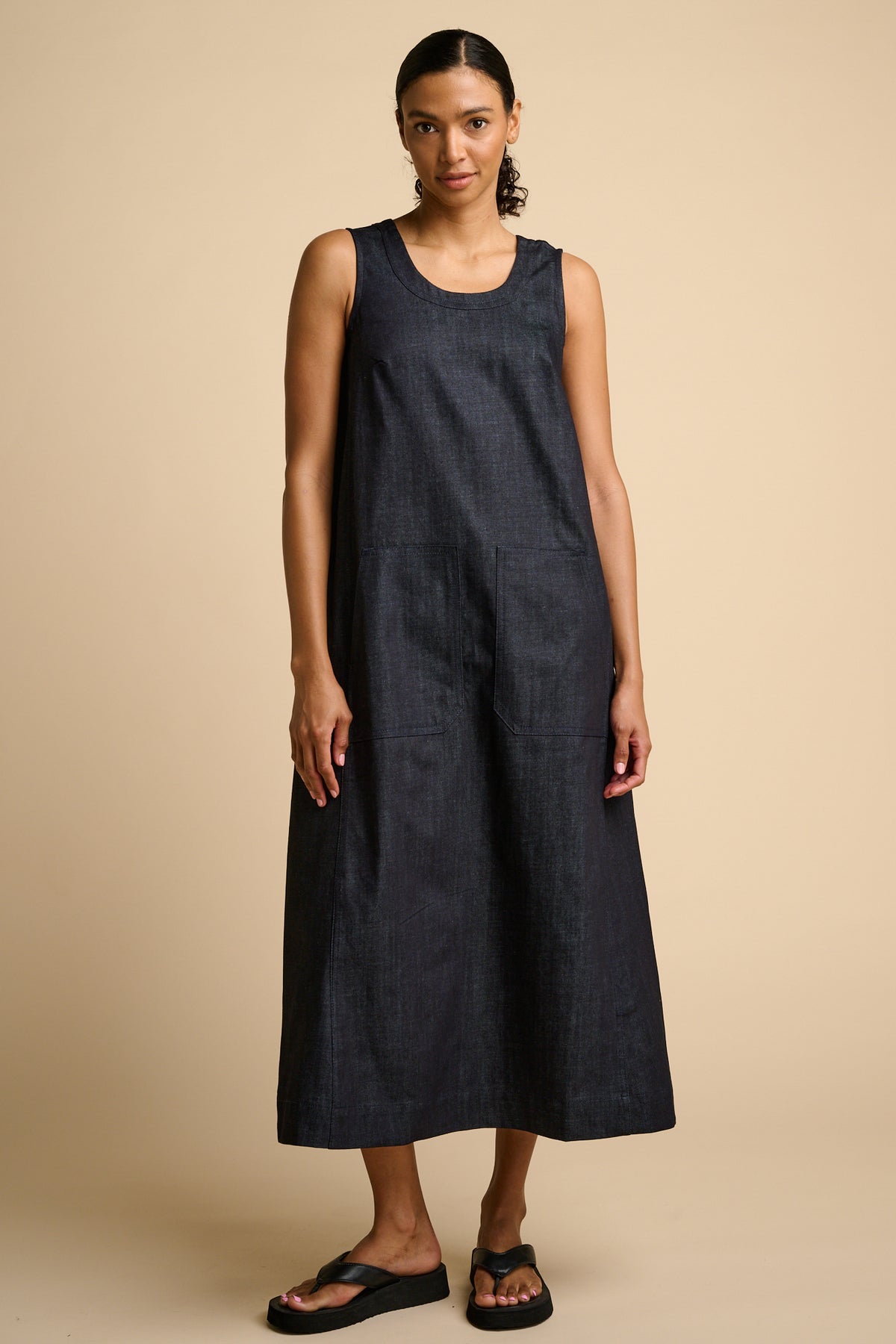 Woman wearing indigo sleeveless dress against a beige background.