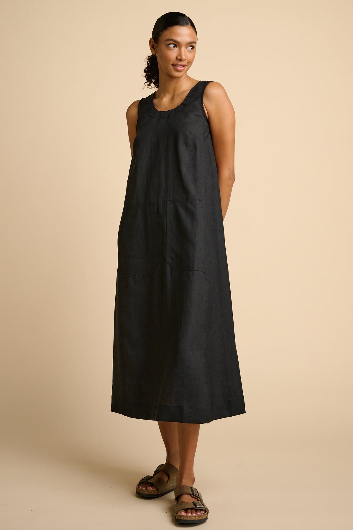 Woman wearing a black sleeveless dress on a beige background.