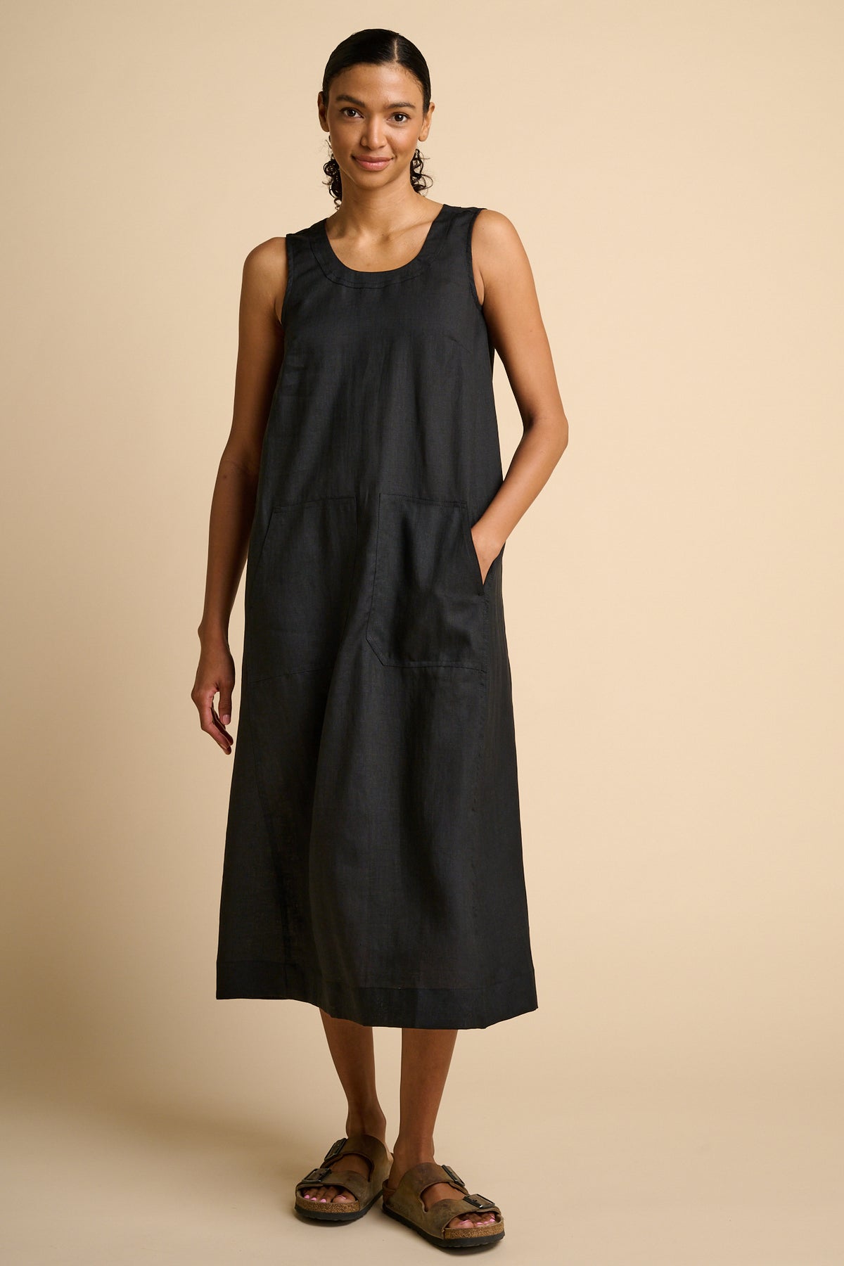 Woman wearing a black sleeveless dress on a beige background.