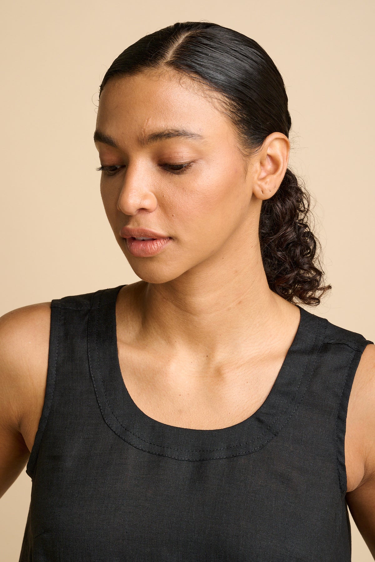 Woman wearing a black sleeveless dress against a beige background.