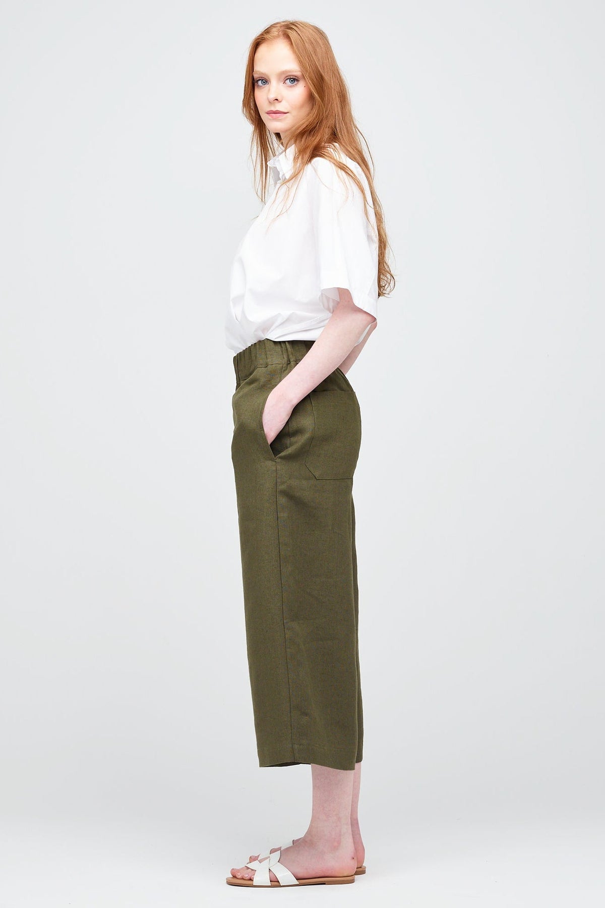 Side shot of a young white women with ginger hair wearing short pj trouser in a khaki coloured linen, styled with an oversized white shirt and sandal.