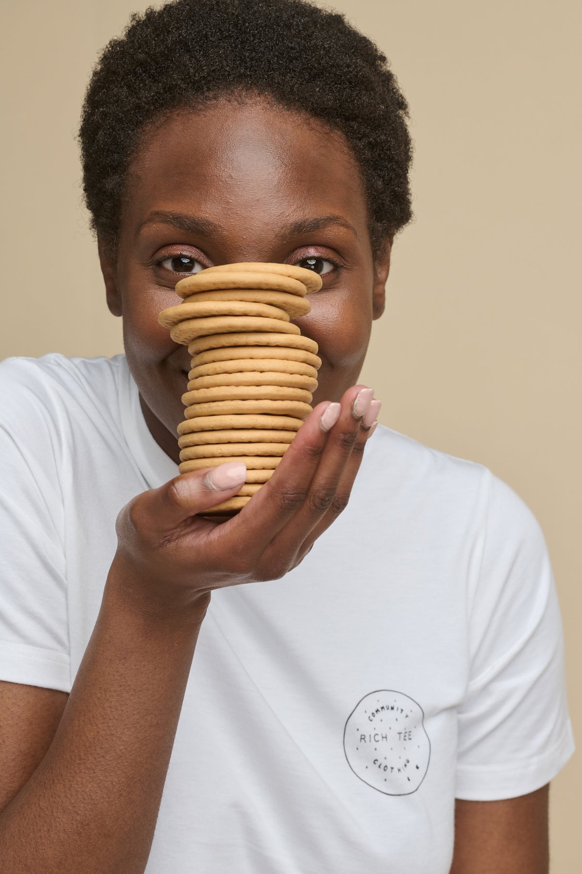 Portrait of female holding a pile of rich tea biscuits wearing short sleeve t shirt in white with ''rich tee'' graphic print on the chest