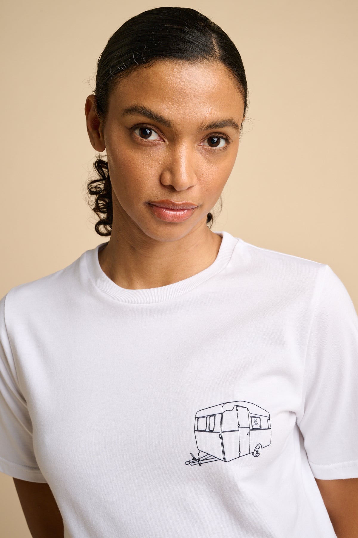 Woman wearing a white t-shirt with a black graphic design on a beige background.