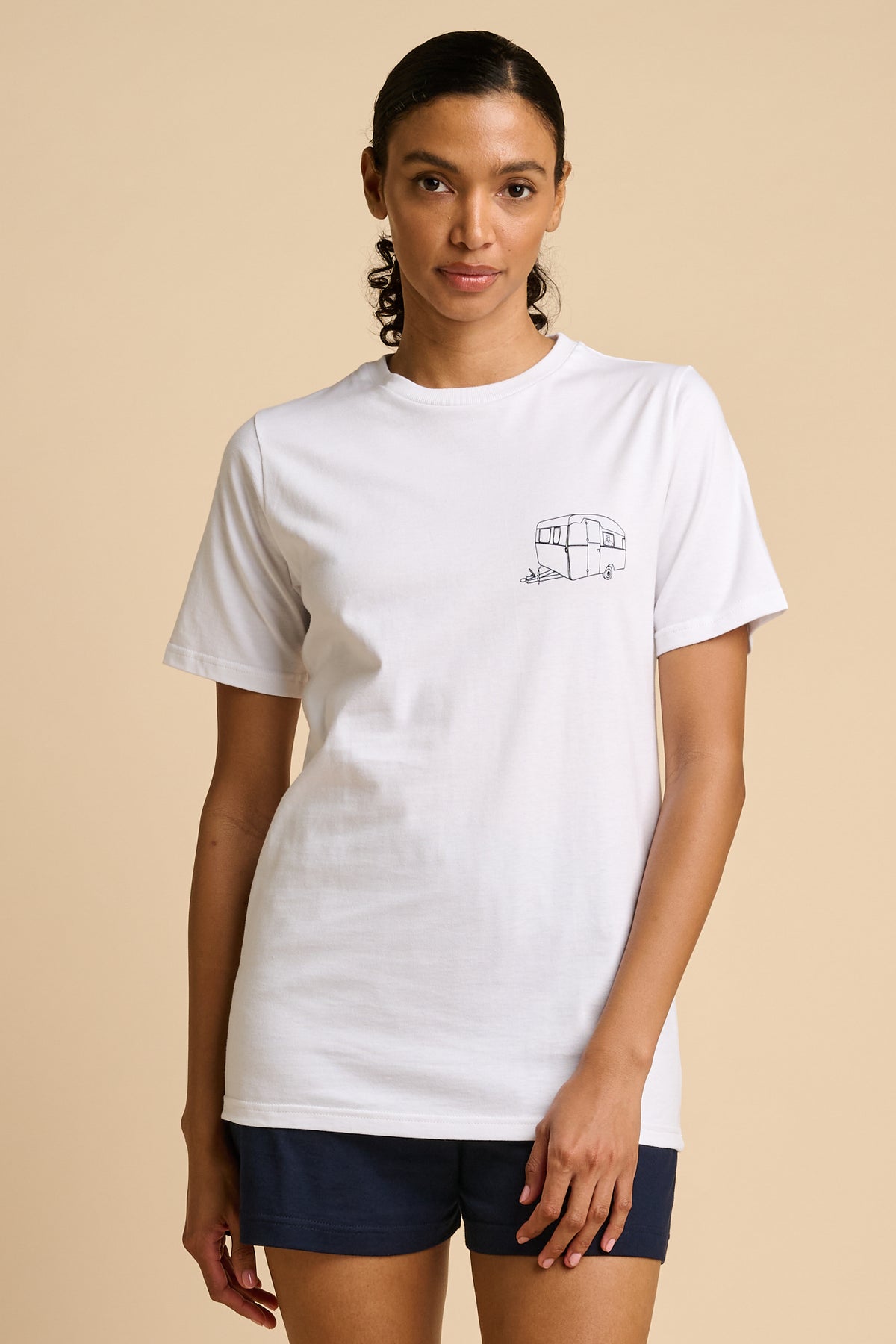 Woman wearing a white t-shirt with a small graphic on a beige background.