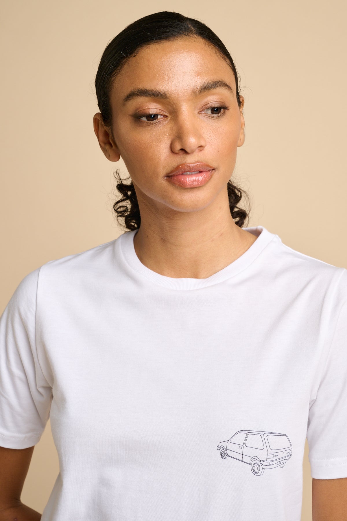 Woman wearing a white t-shirt with a small graphic on a beige background