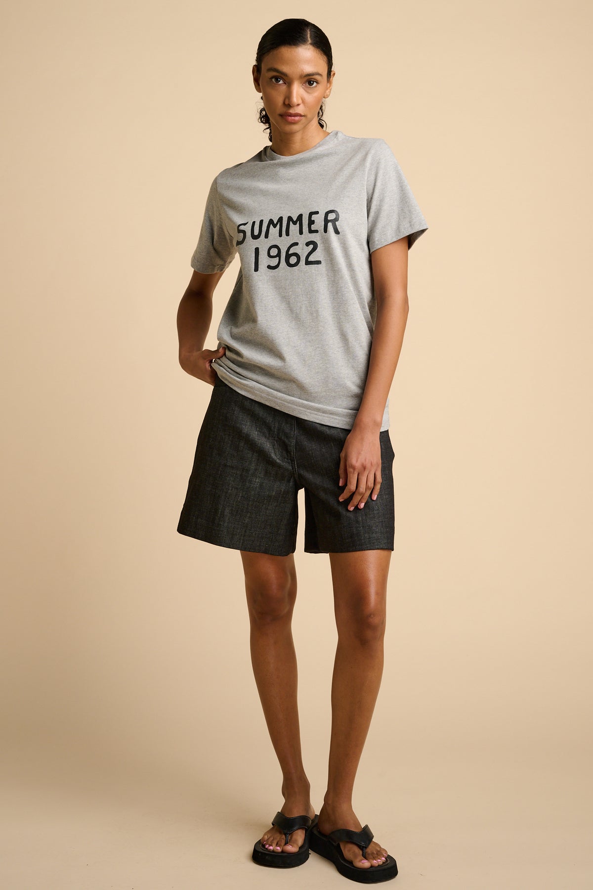 Woman wearing a grey t-shirt with 'SUMMER 1962' text graphic print.