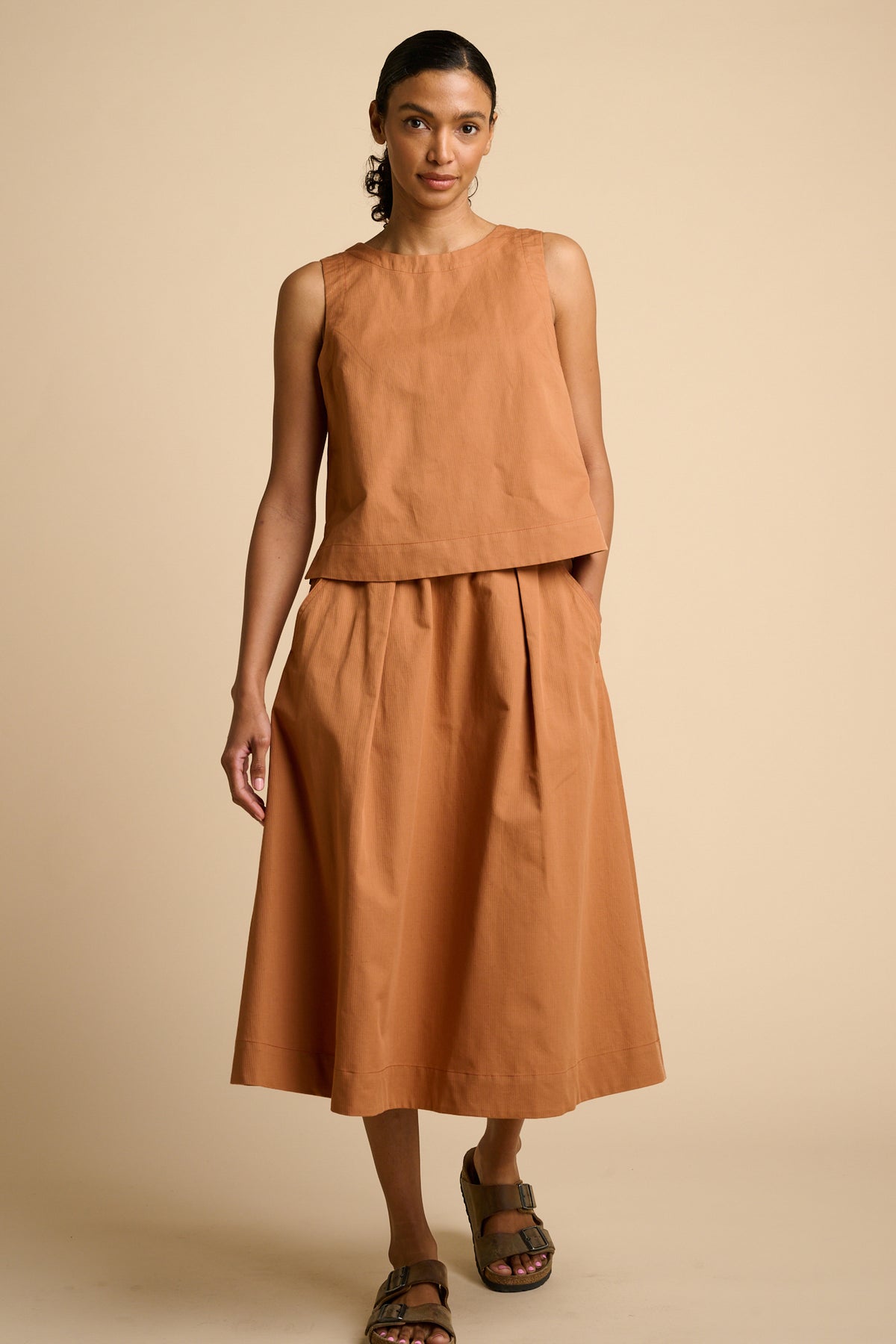 Woman wearing sleeveless orange top and matching skirt.