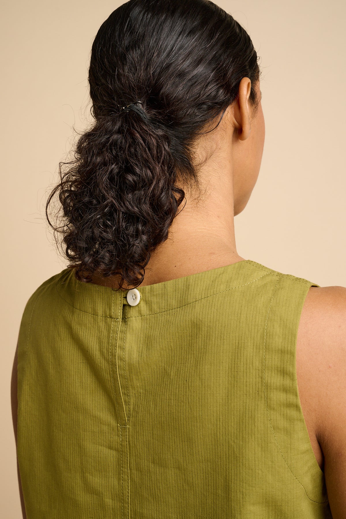 Person wearing a green sleeveless top with a beige background.