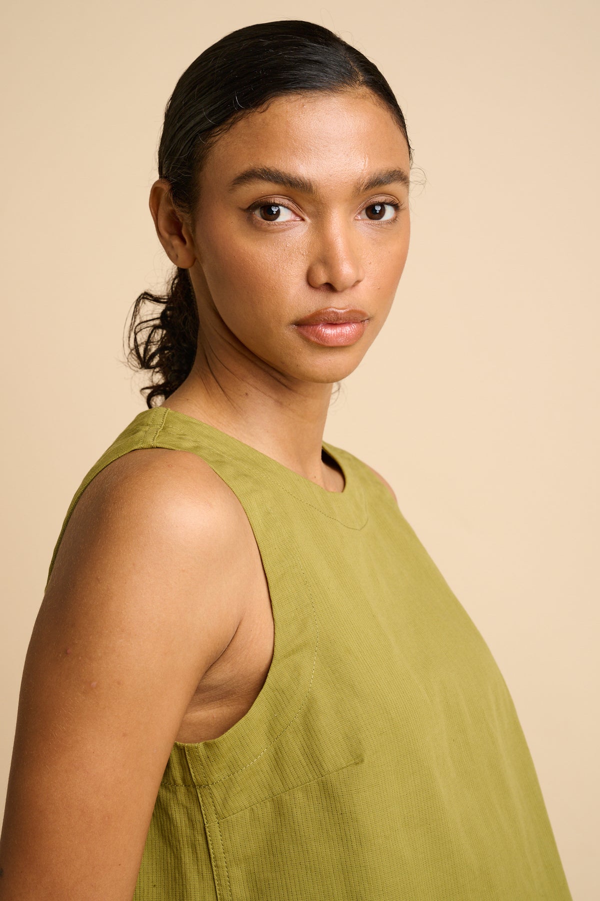 Woman wearing a green sleeveless top against a beige background.