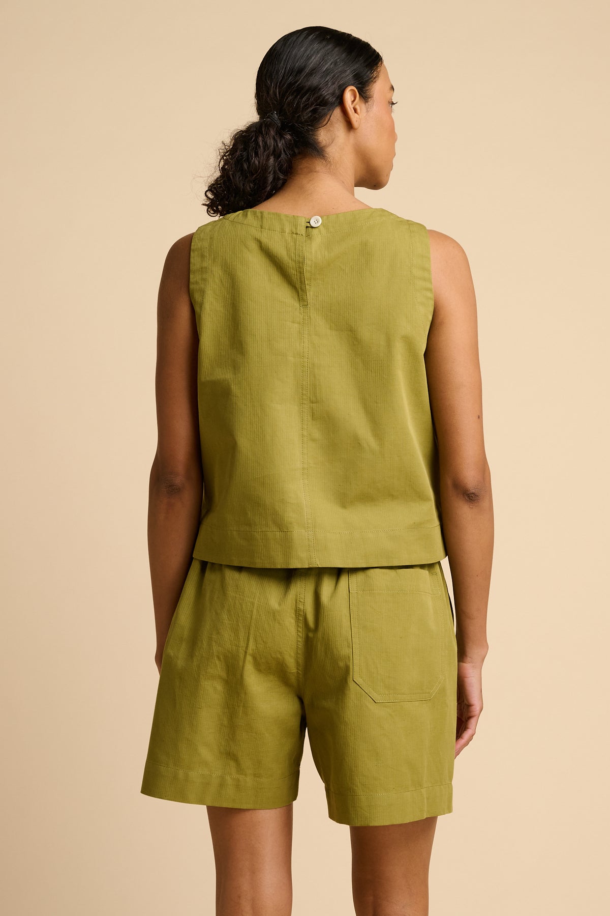 Woman wearing a green sleeveless top and shorts against a beige background.