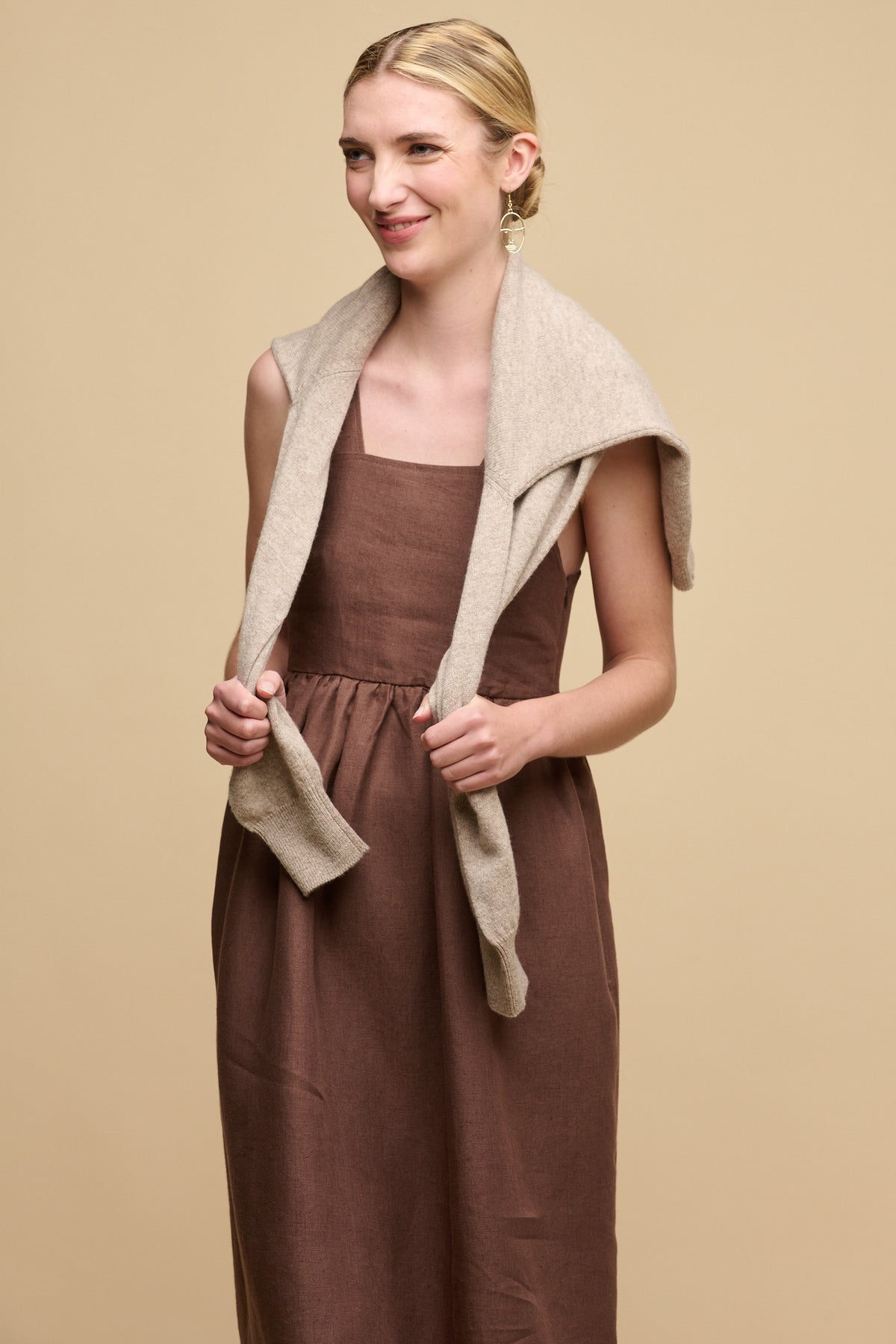 Image of the front of smiley female wearing sun dress in cocoa with lambswool crew neck draped over shoulders