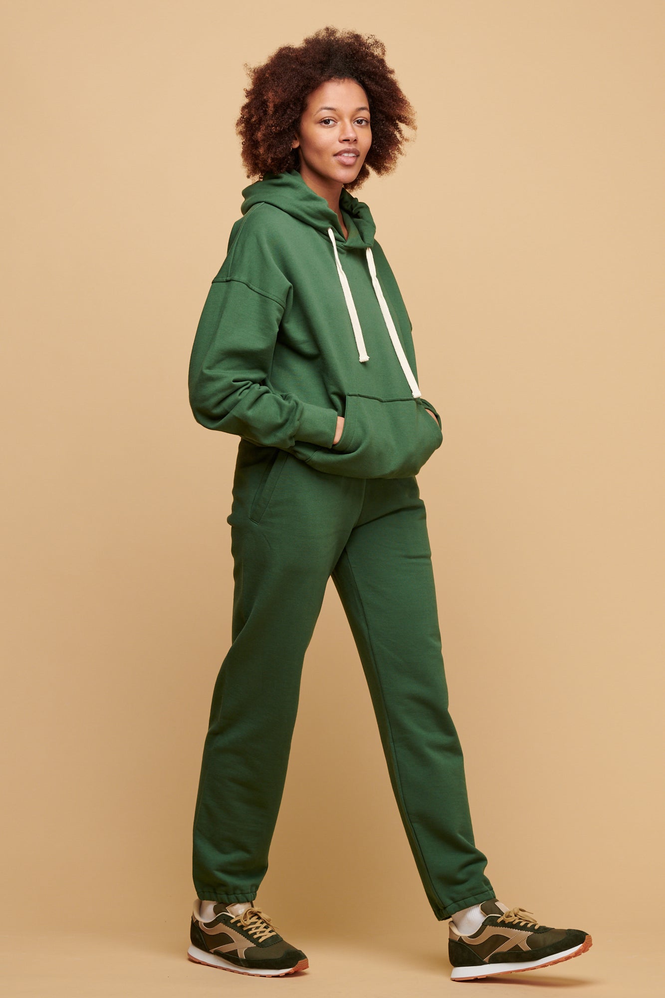 Close up of female wearing women's sweatpants in bottle green with her hand in the front pocket, elasticated waistband with adjustable ecru drawcord 