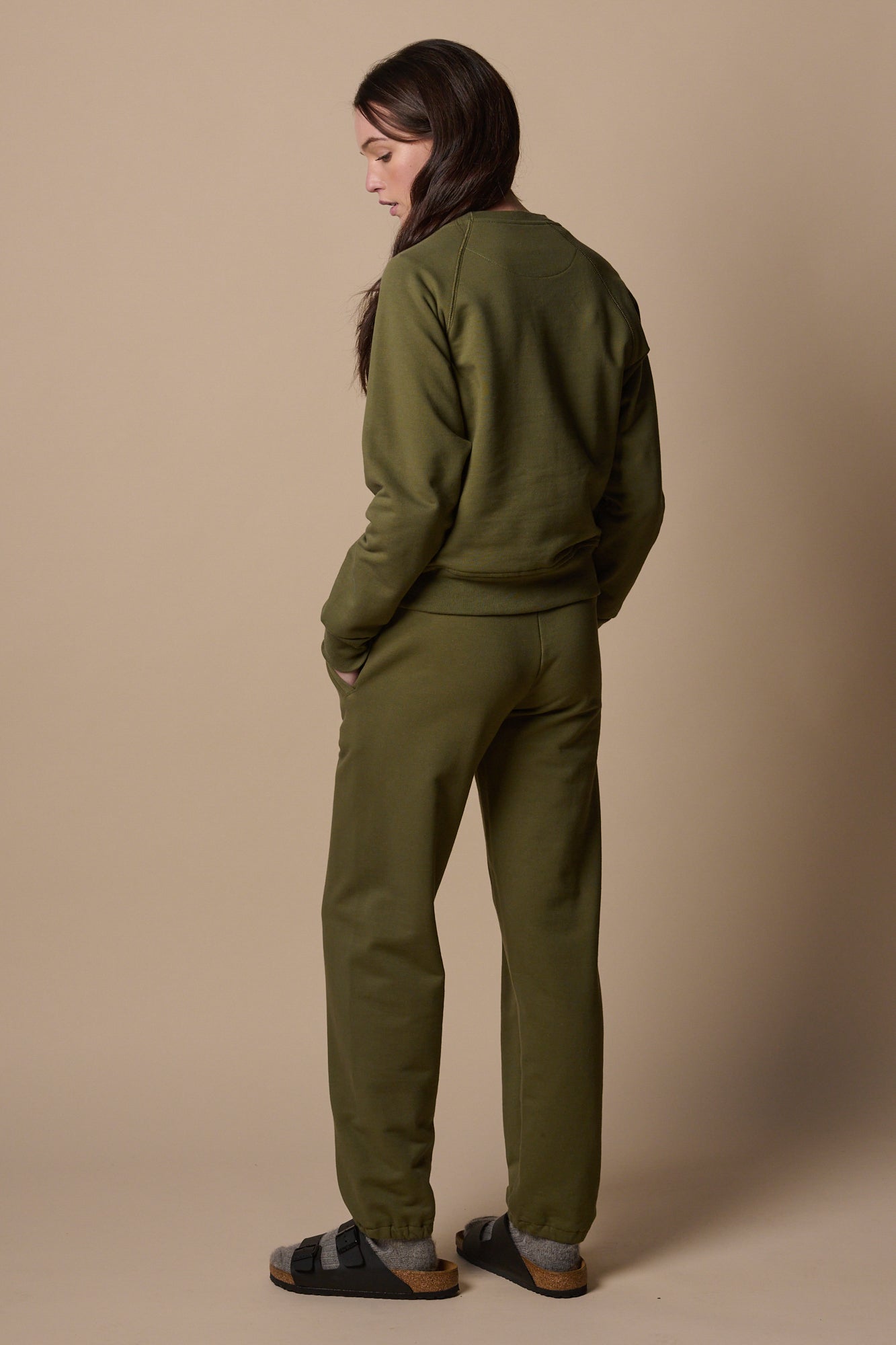 Full body side view of white female wearing sweatpants in olive with matching olive sweatshirt 