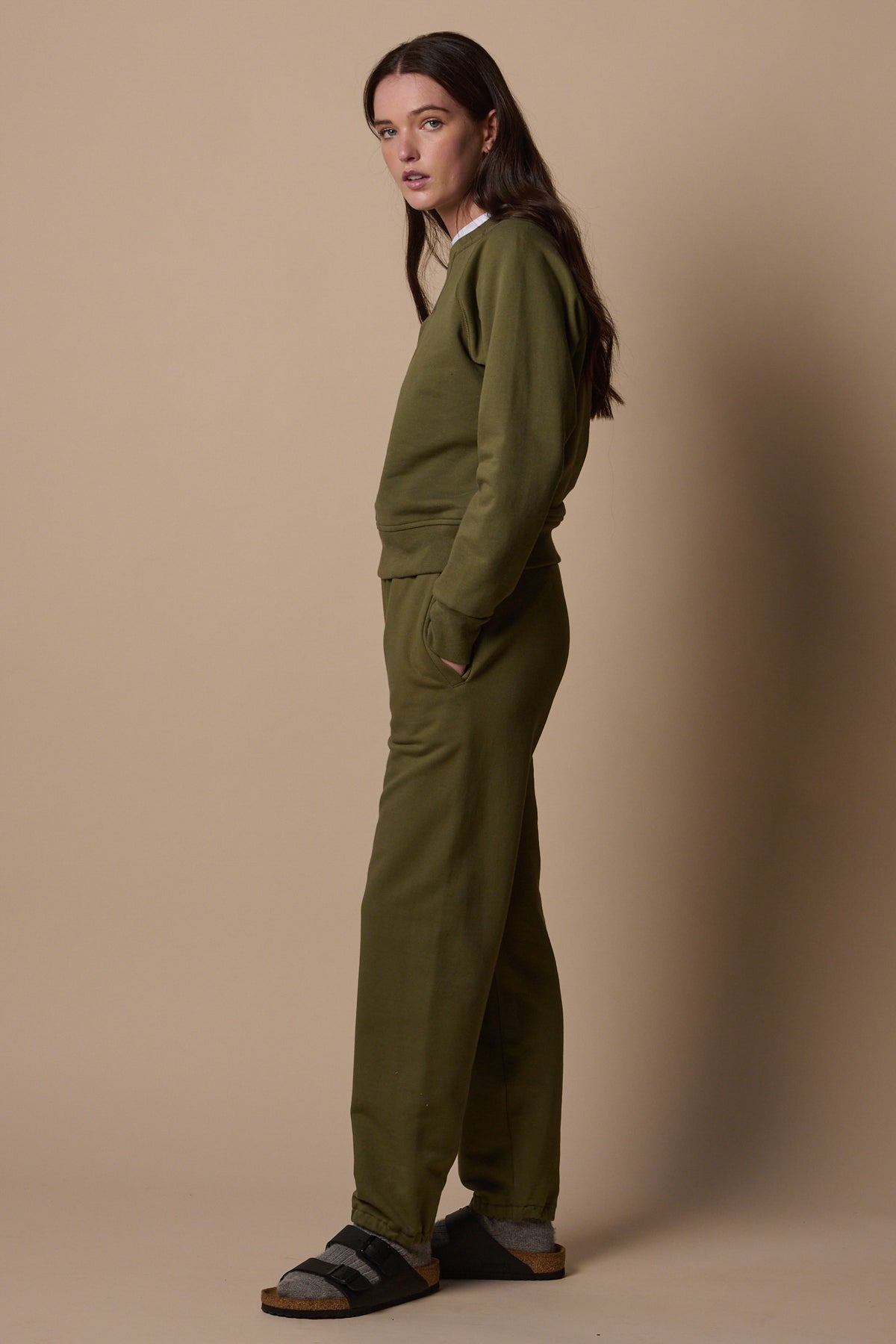 Full body side view of white female wearing sweatpants in olive with matching olive sweatshirt 