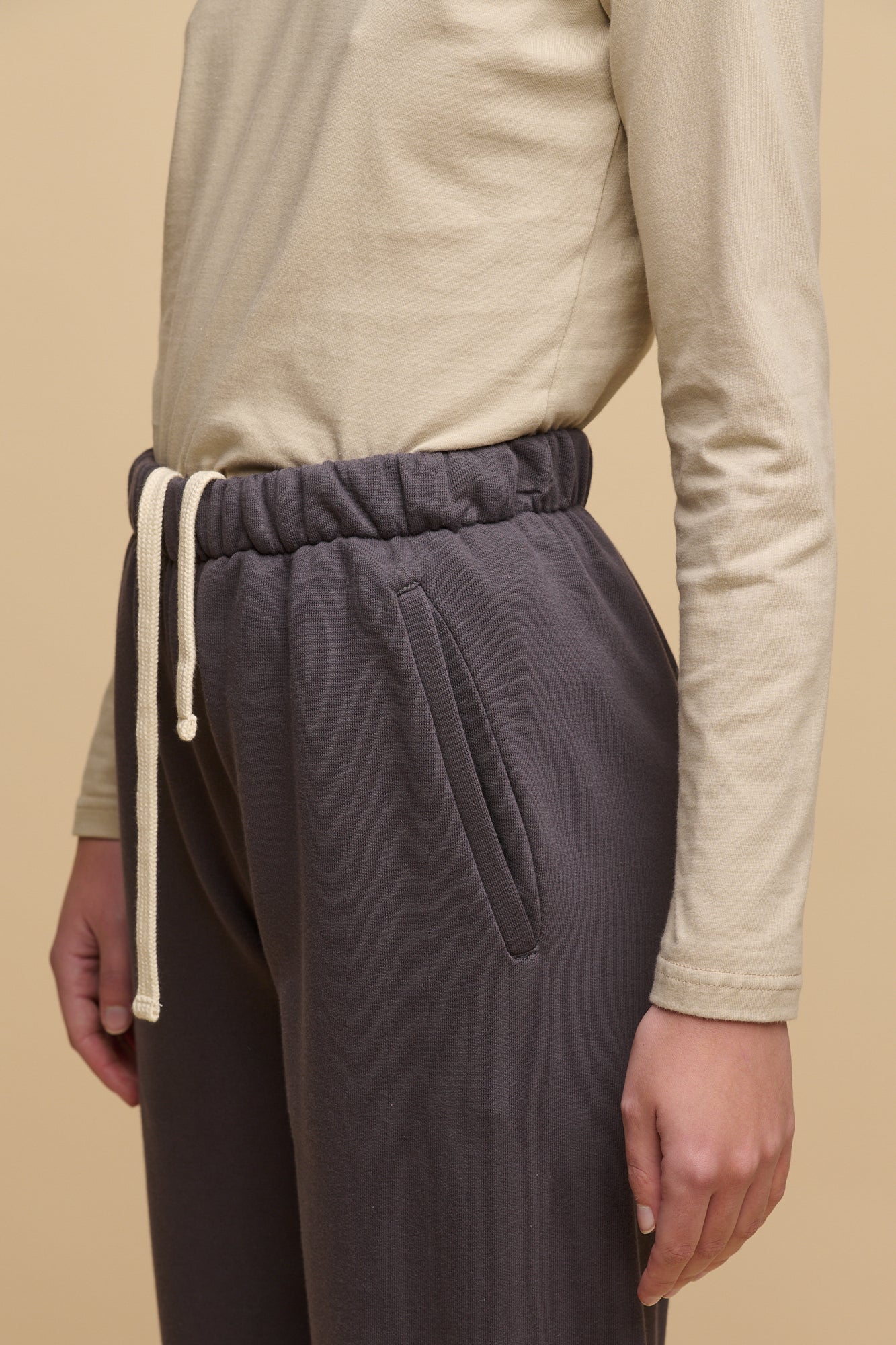 Waist down image of female wearing sweatpants in slate grey with hands in front pockets and ecru drawstring for waist out at the front. Worn with long sleeve t shirt in stone tucked in and cushioned wool walking socks in fawn