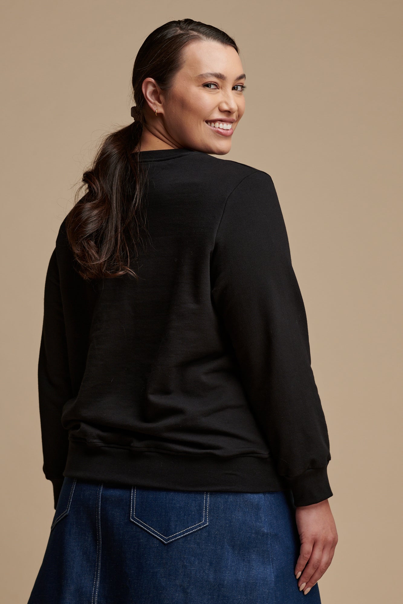 Thigh up of female wearing sweatshirt in black paired with bobbie skirt in blue.