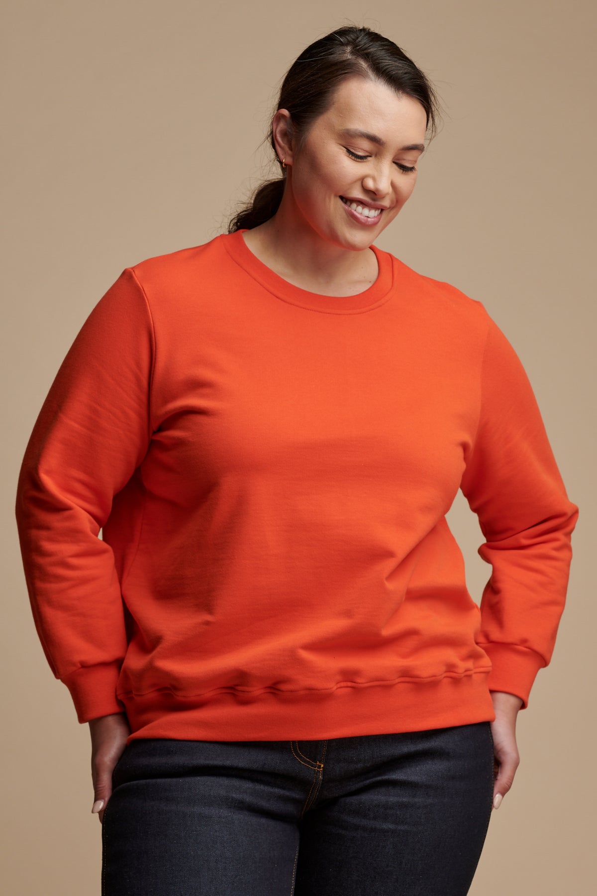 Smiley female looking towards the ground  wearing sweatshirt in flame red.
