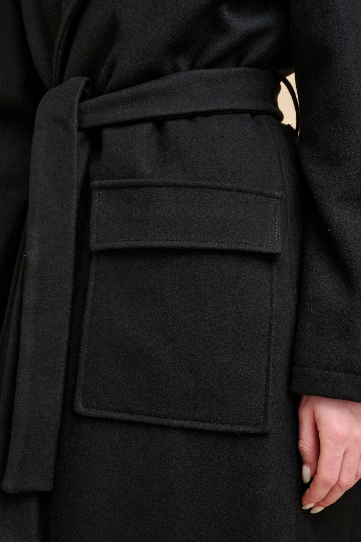 Close-up of a black coat with a belt and large front pockets.