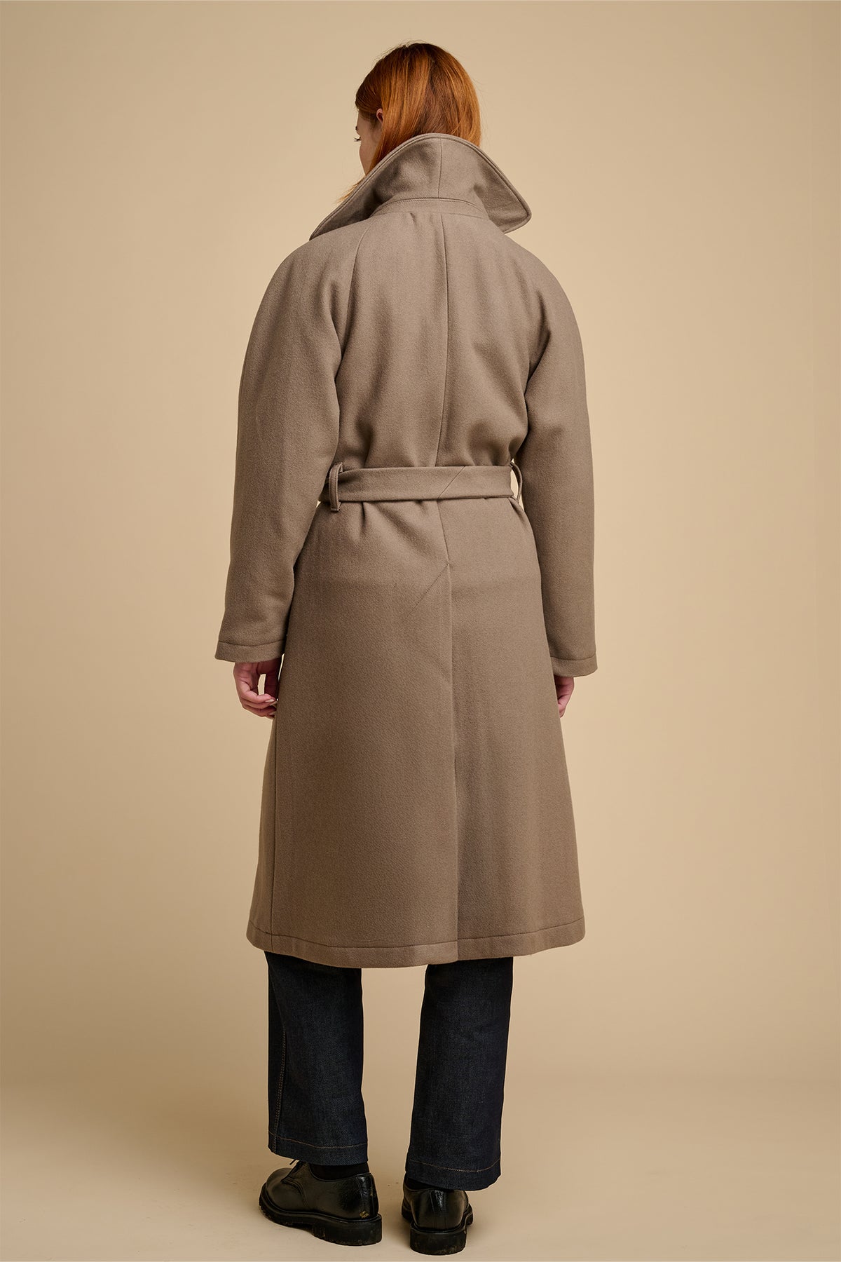 The back of woman beige wearing long wool coat against beige background.