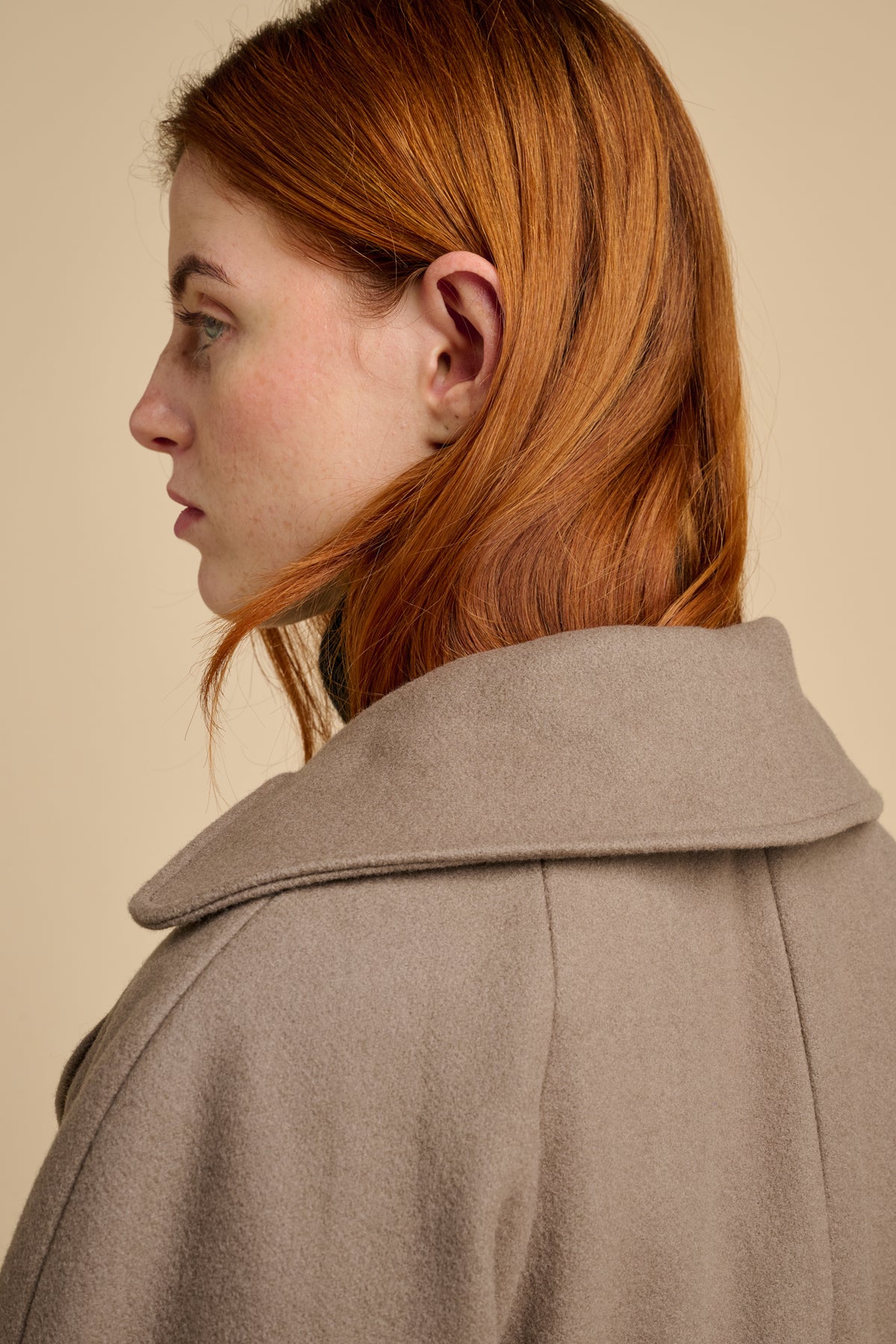 The back of woman wearing a beige long wool coat against a beige background