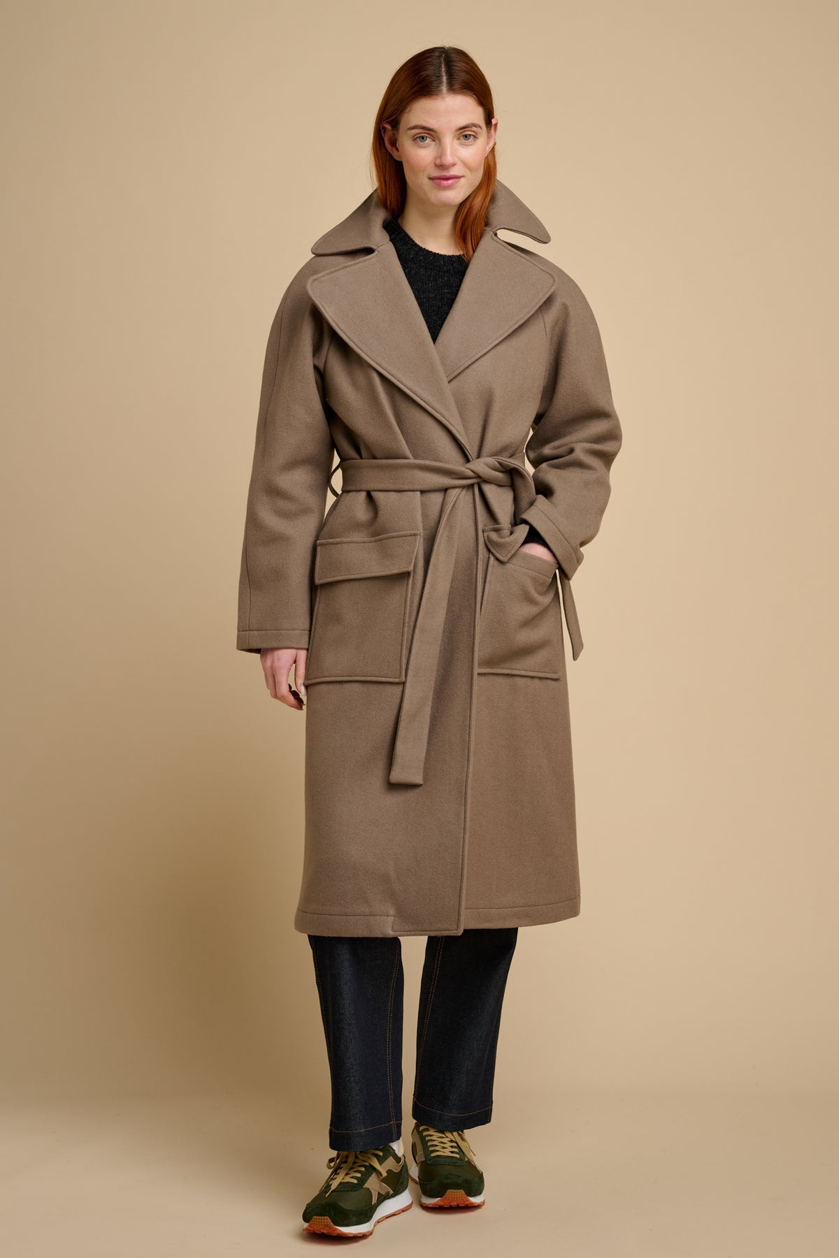 Woman wearing a beige long wool coat against a beige background