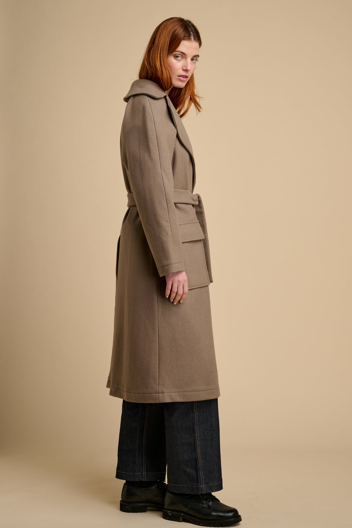 Woman wearing a beige long wool coat against a beige background