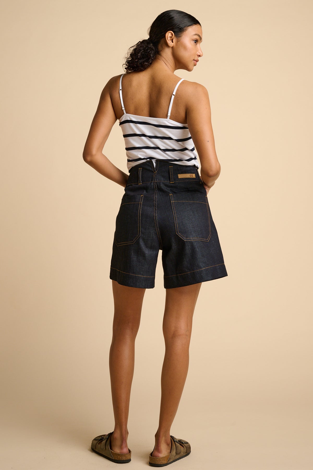 Woman wearing a striped tank top and denim shorts on a beige background