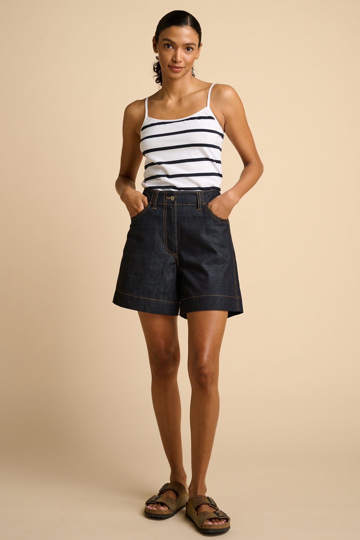 Woman wearing a striped tank top and denim shorts on a beige background
