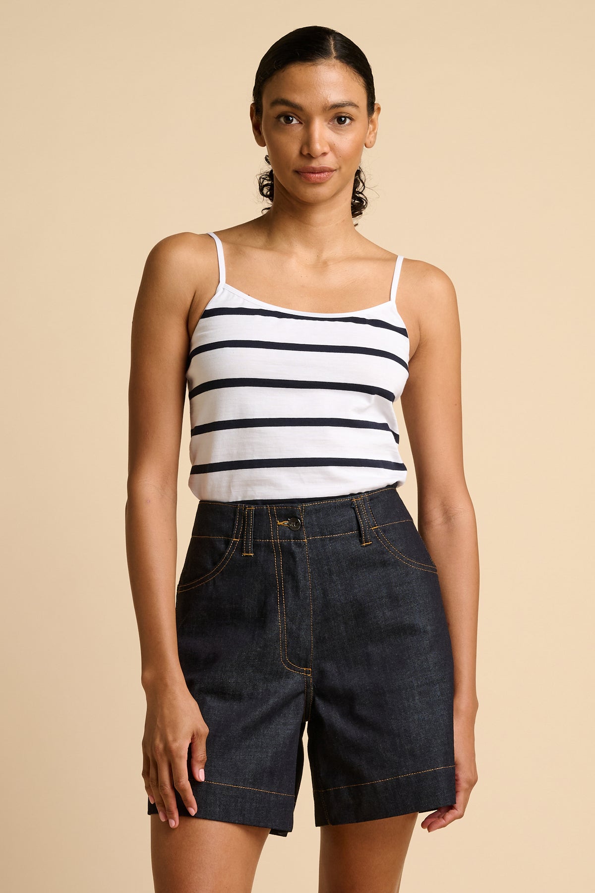 Woman wearing a striped tank top and denim shorts on a beige background