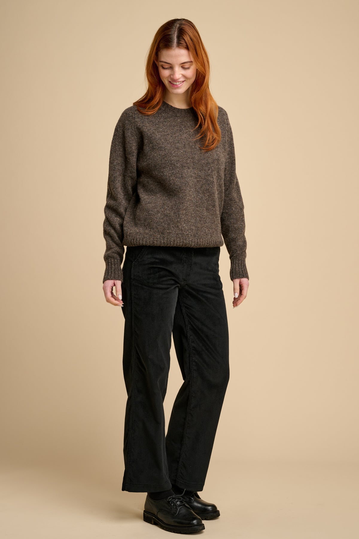 Woman wearing a brown sweater and black pants on a beige background