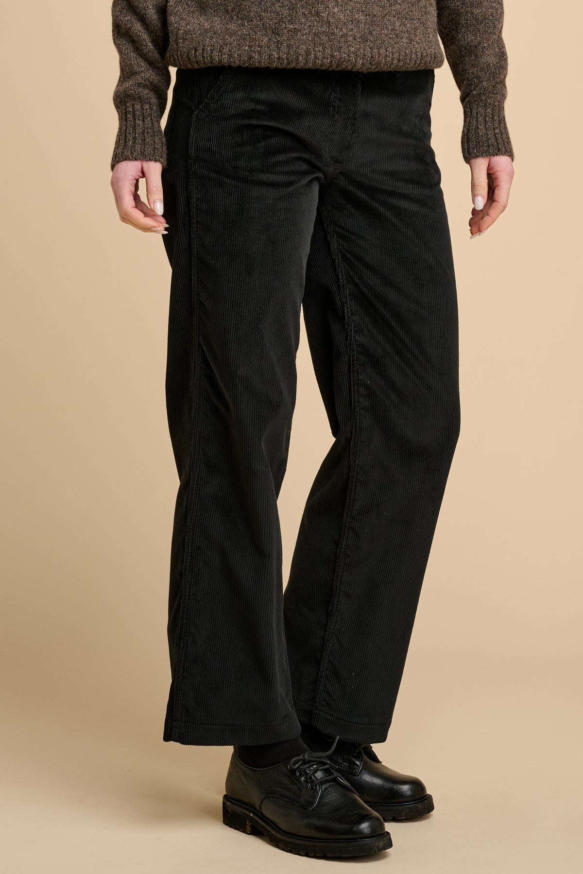 Woman wearing black corduroy trousers against beige background.