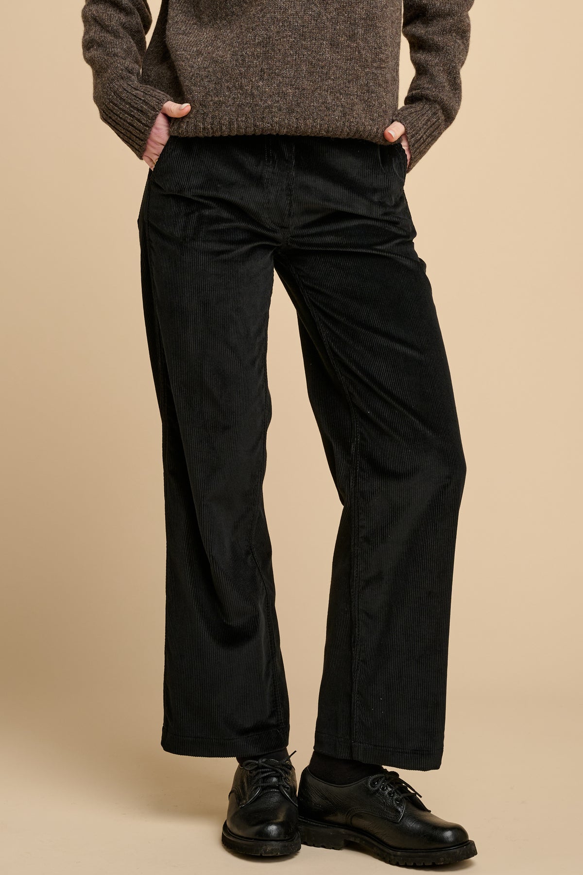Woman wearing black corduroy trousers against beige background.