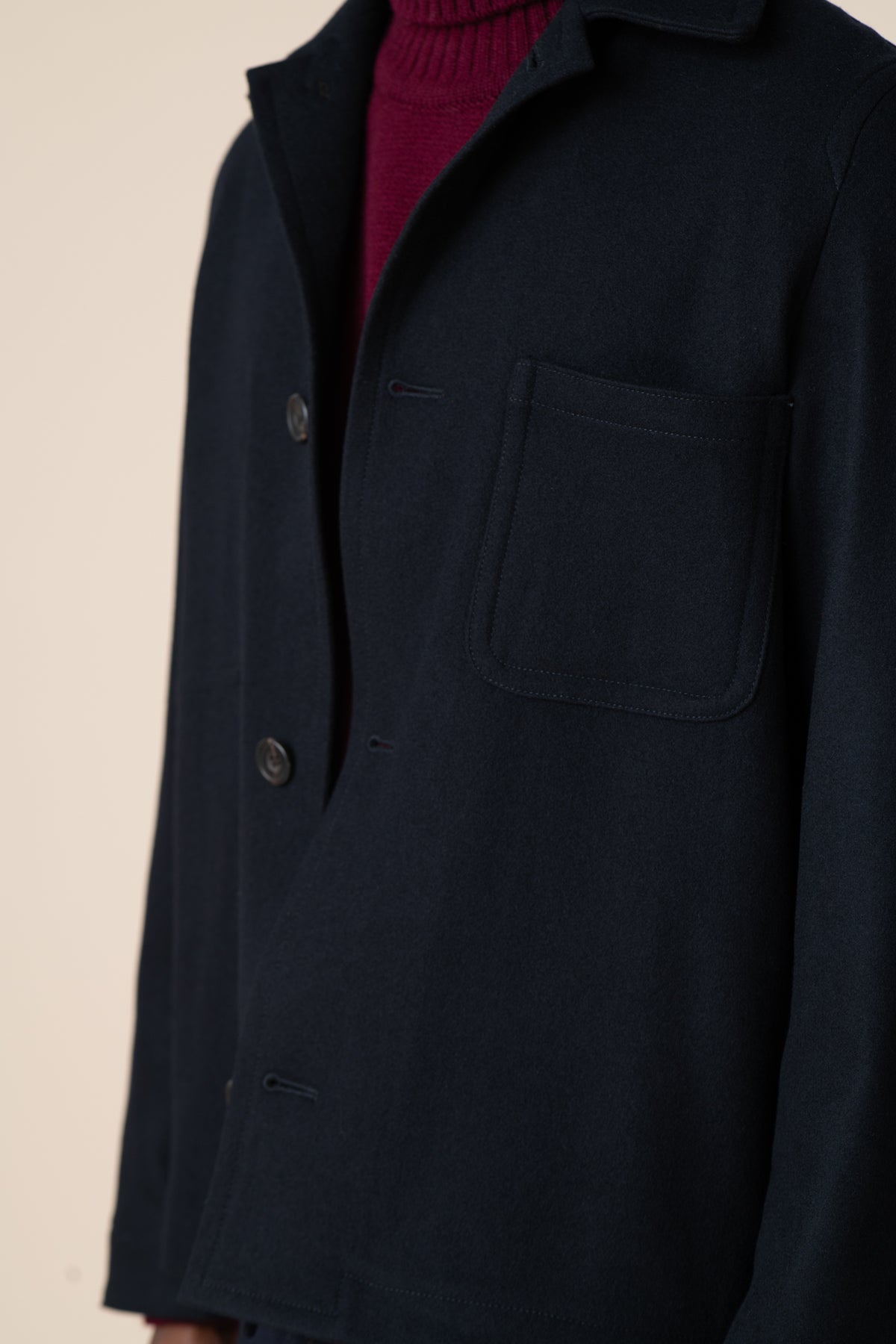 Detail image of top pocket of Arthur wool chore jacket in navy, layered over lambswool roll neck in burgundy.