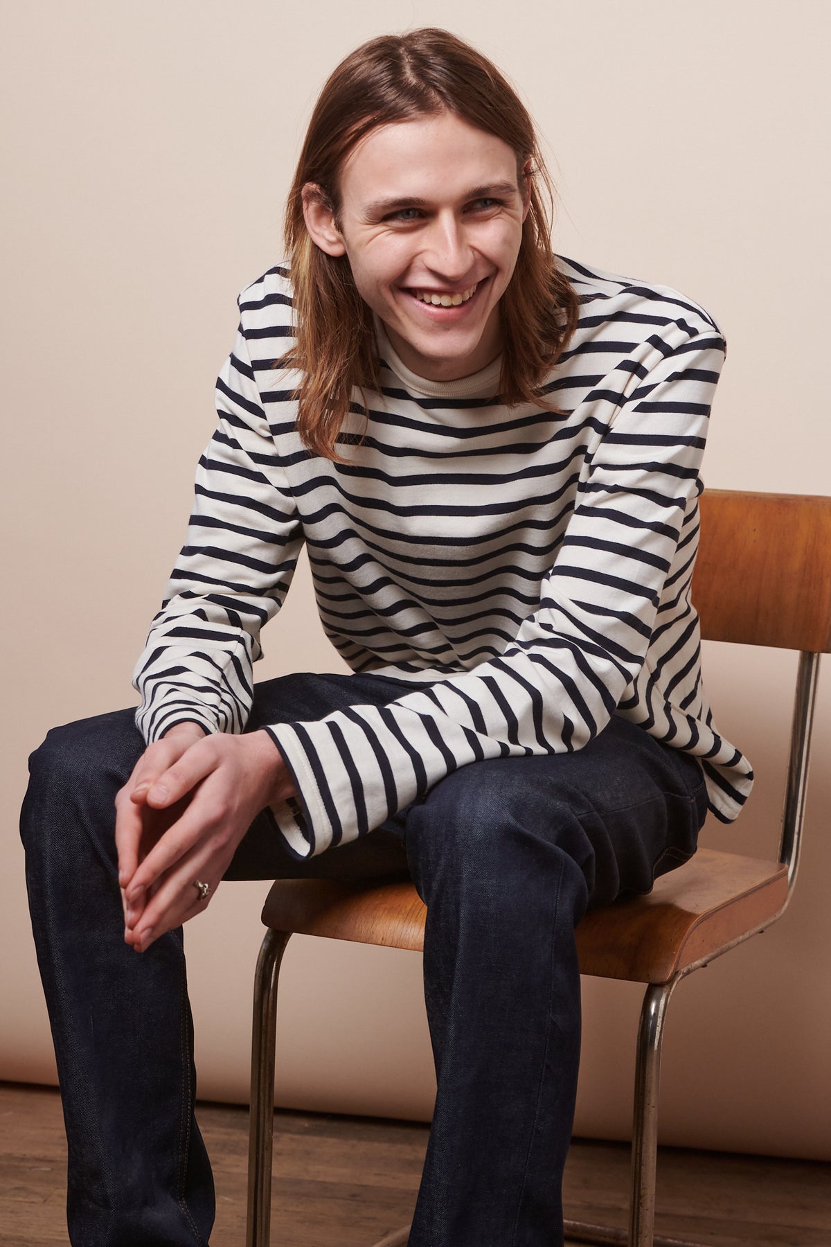 Smiley male with shoulder length brown hair sat on chair wearing Breton in ecru navy