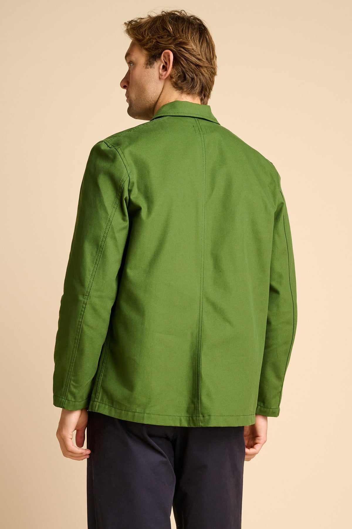 Man wearing green chore jacket against beige background.