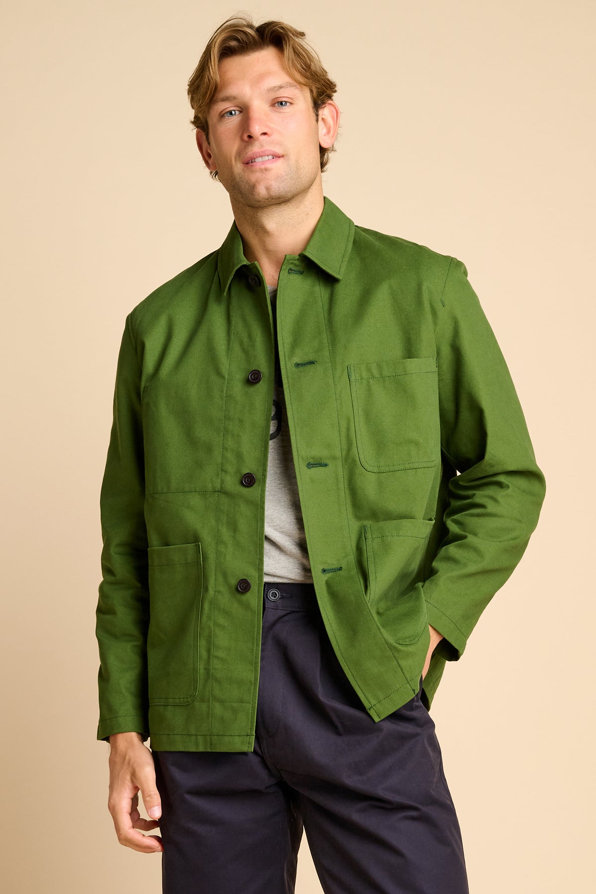 Man wearing green chore jacket against beige background.