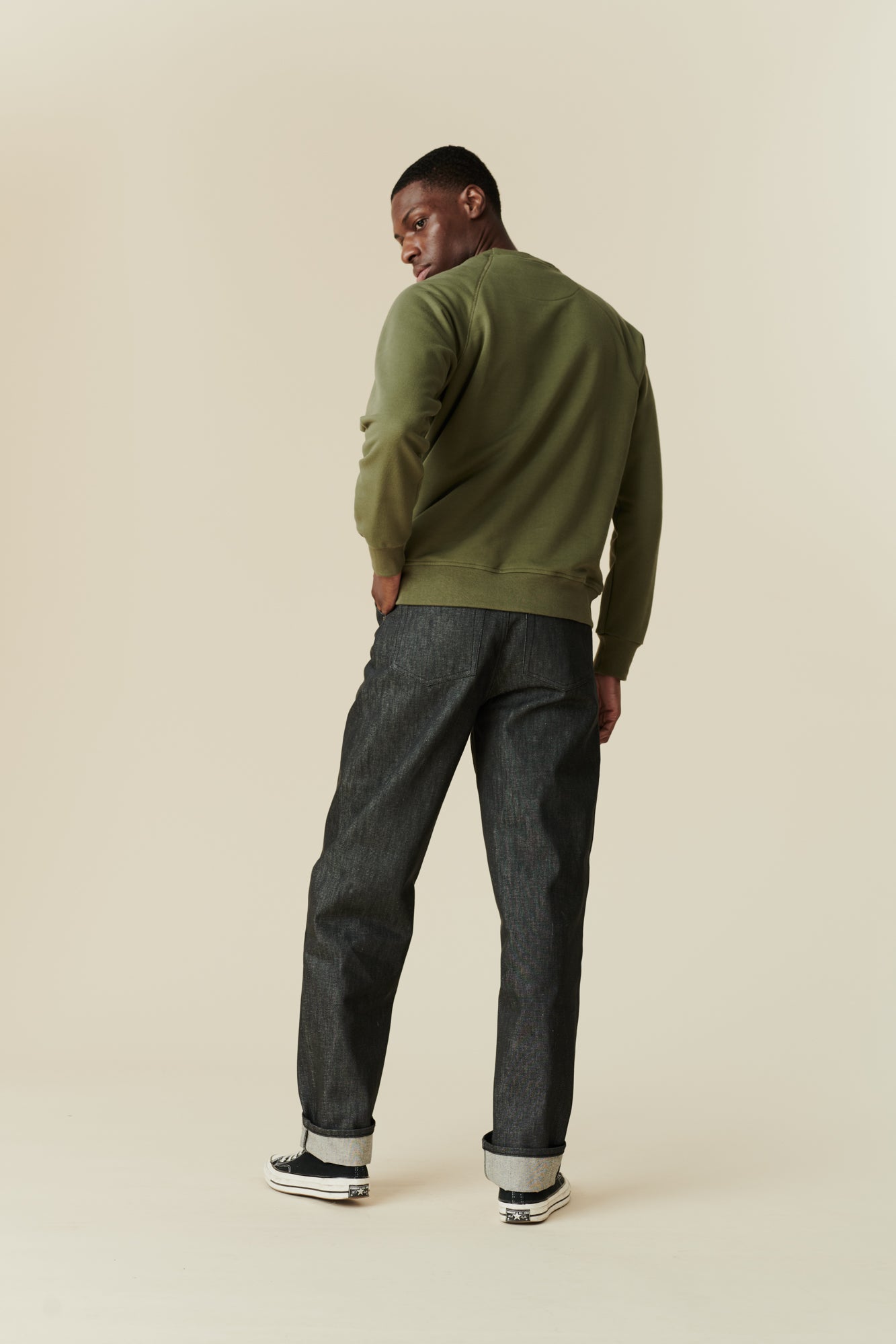 Black male wearing men's Chore jeans in black, wide leg and tapered fit with rolled hem, worn with olive green raglan sweatshirt