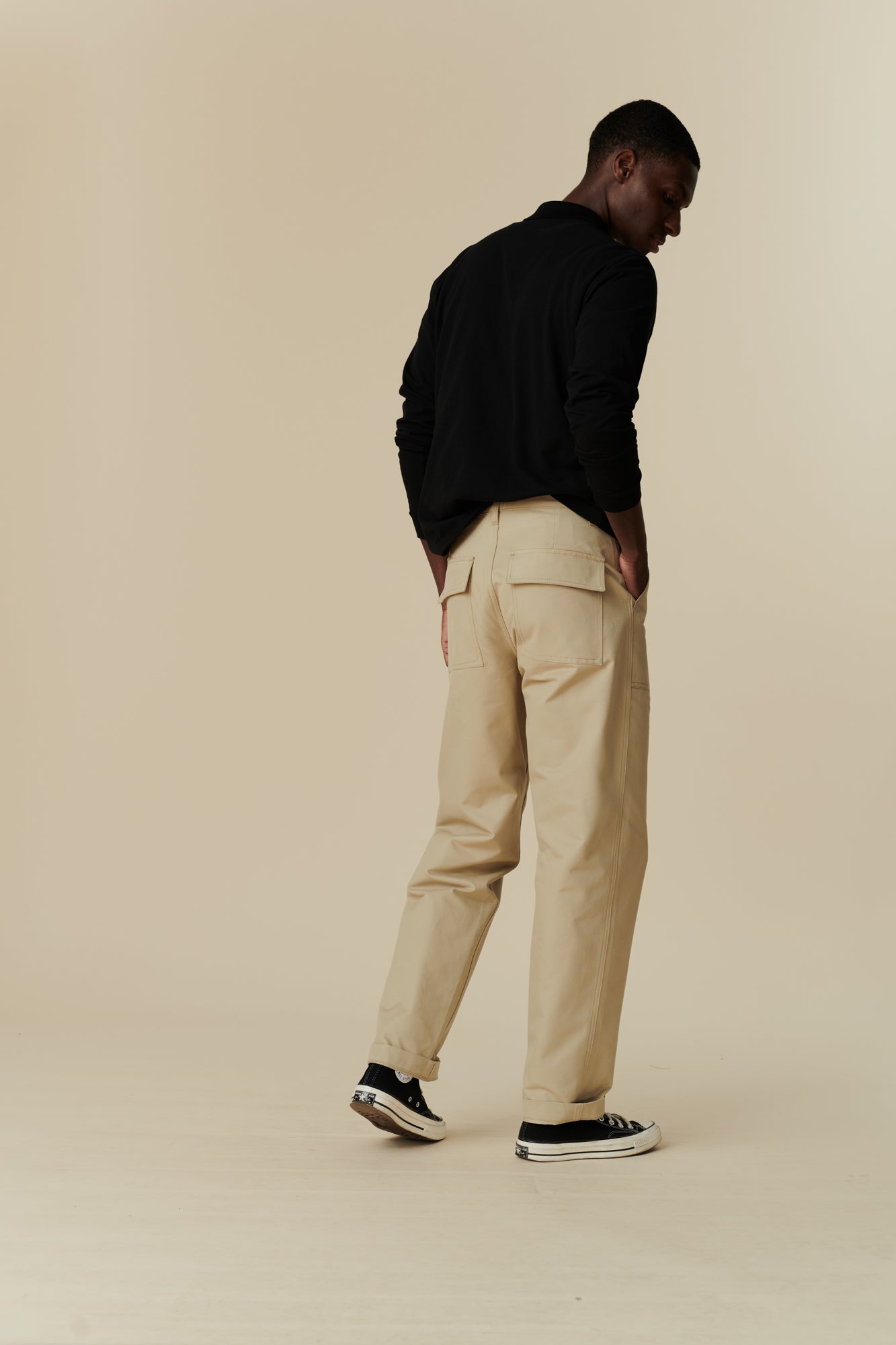 Full body image of black male wearing combat trouser in putty, worn with long sleeve polo shirt in black